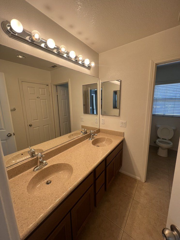 A bathroom with two sinks , two mirrors and a toilet.