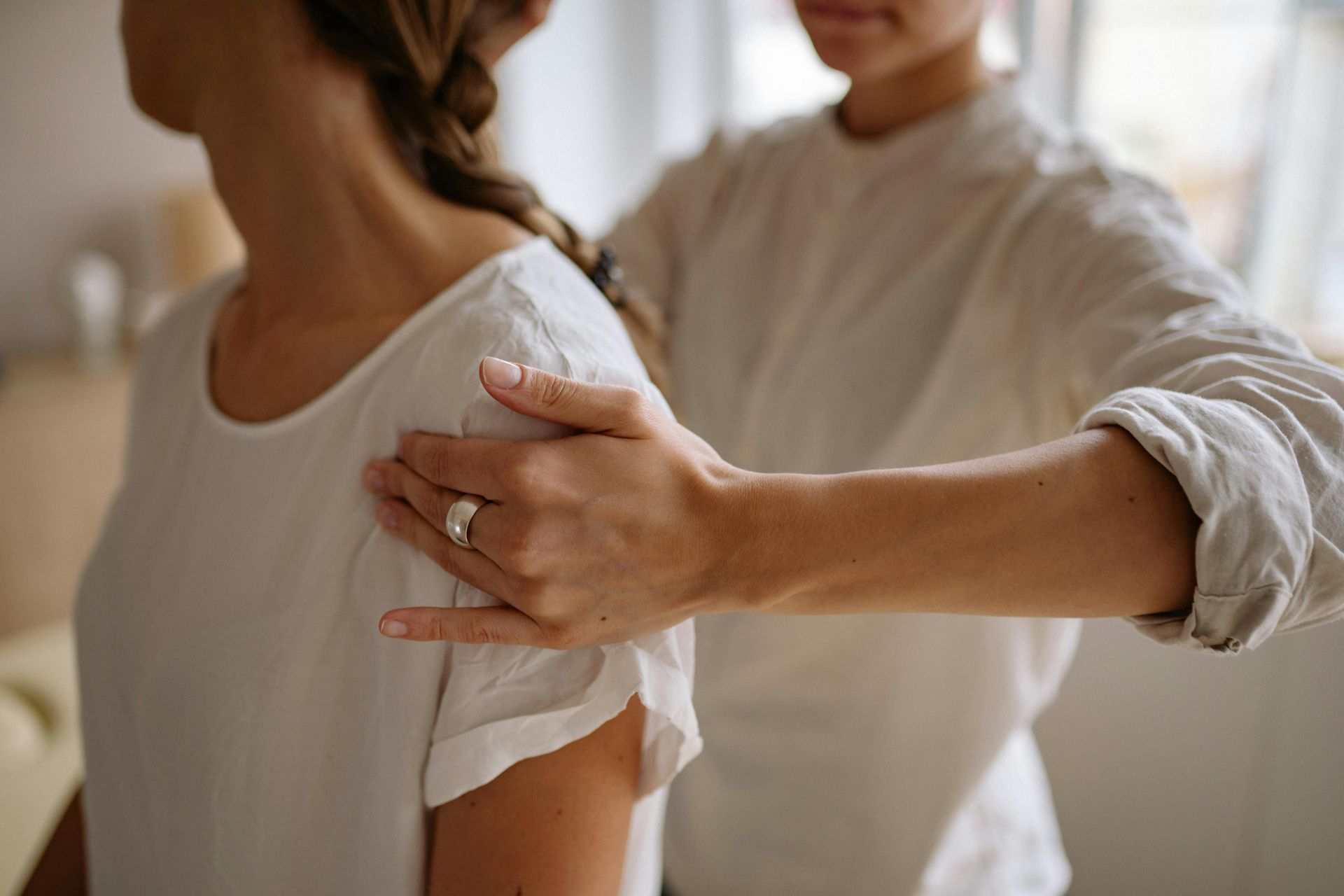 Person's shoulder being gently touched by another person's hand, soft lighting, white shirts.