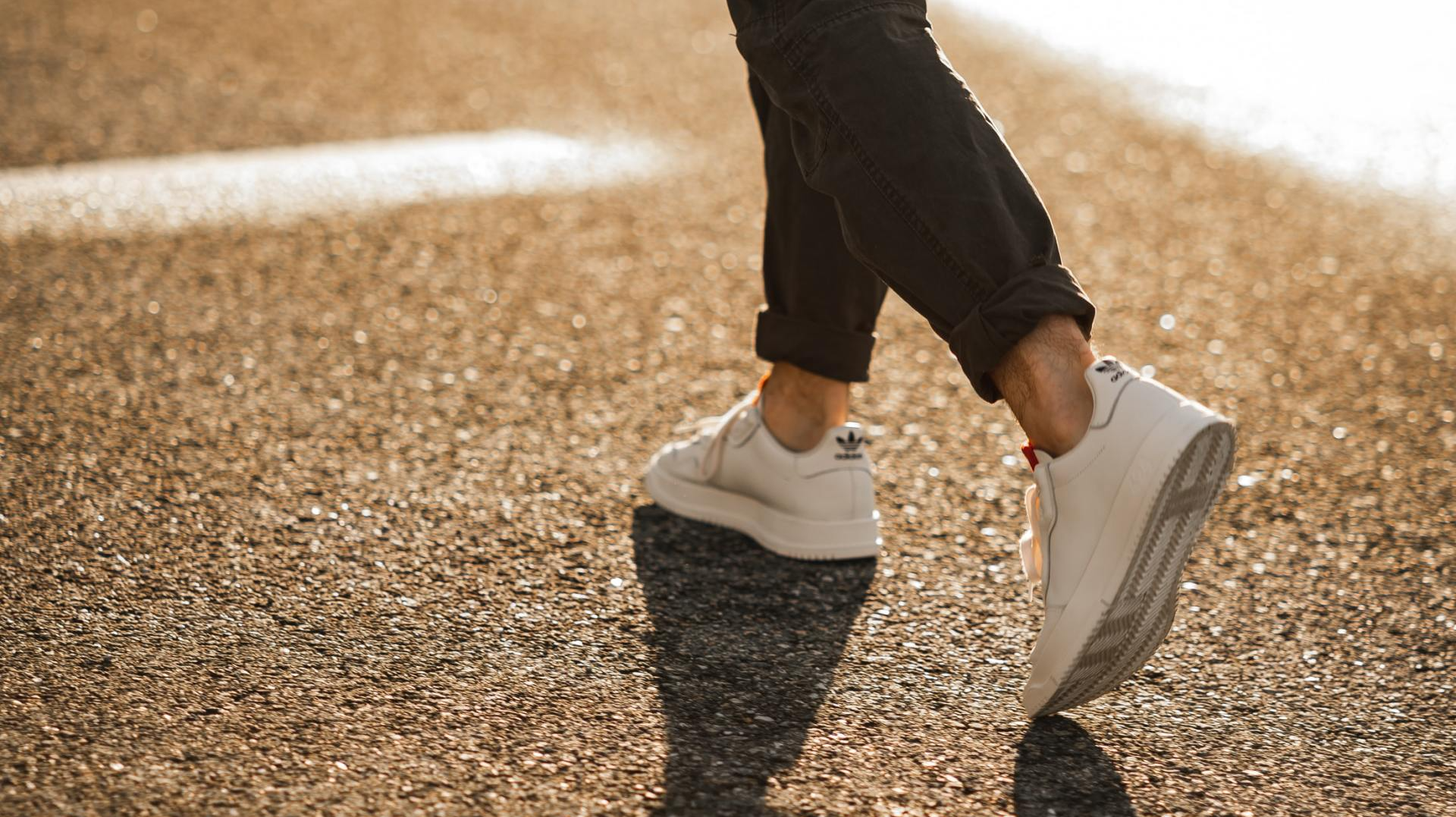 een persoon die witte sneakers draagt, loopt op een weg.