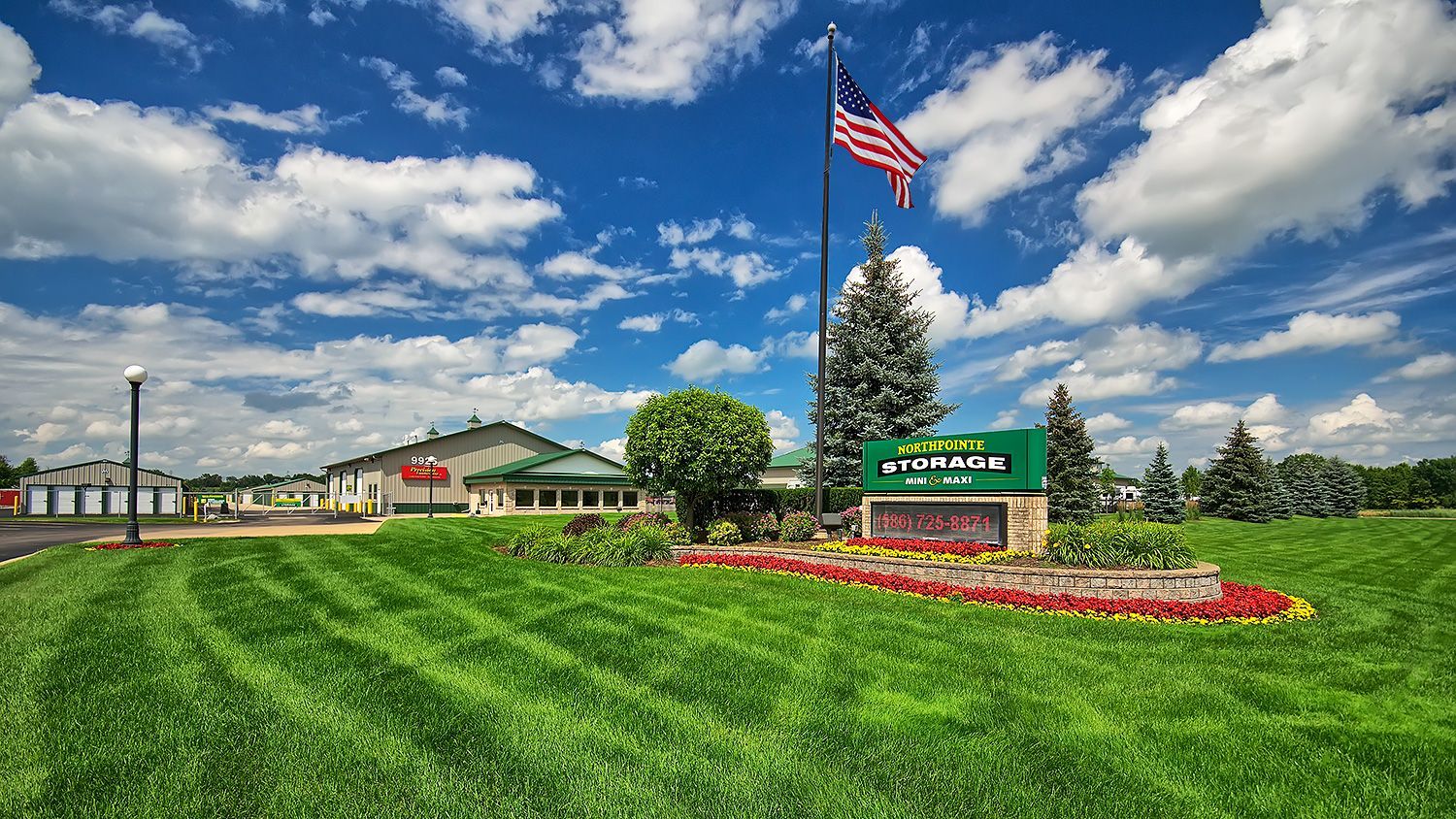 Green lawn and flower bed before a U.S. flag and park entrance sign under a blue sky