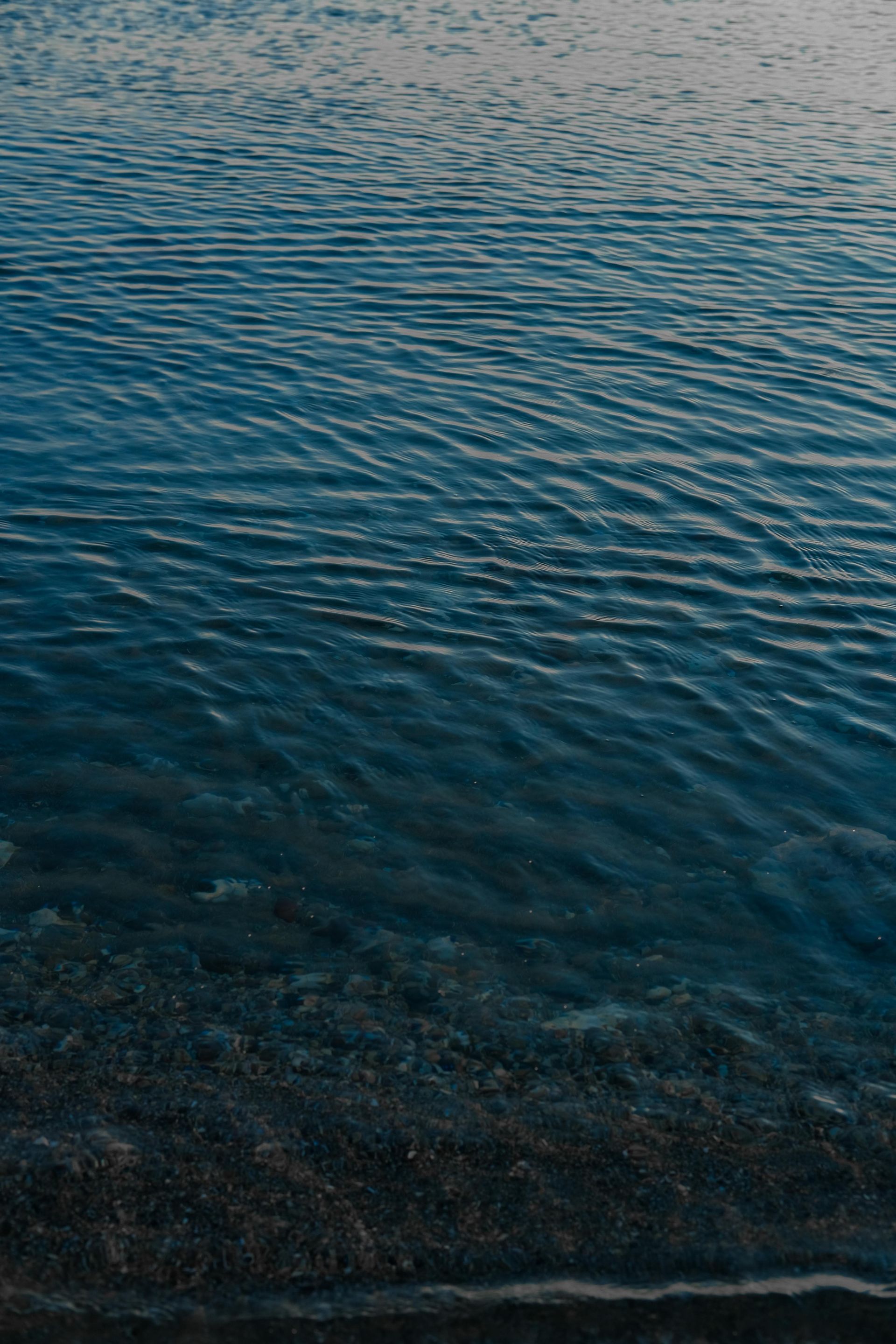 Calm blue water with gentle ripples, viewed from above near a rocky shoreline