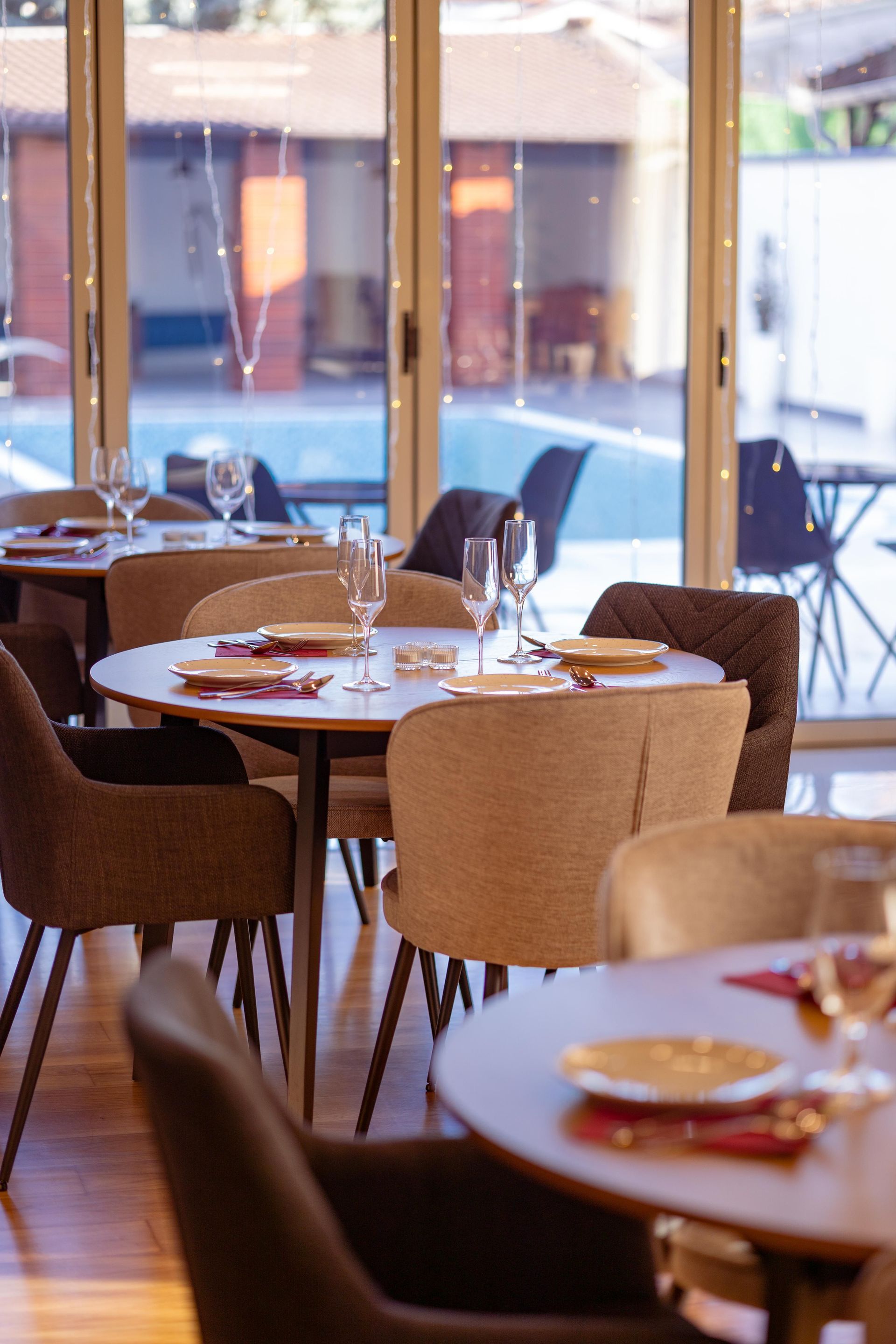 Empty café with wicker chairs, round tables, and large windows overlooking an outdoor patio.