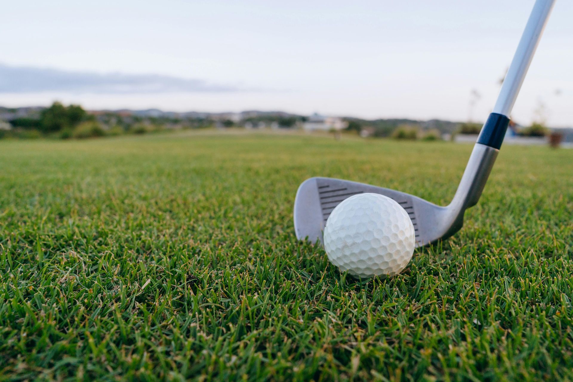 Golf ball beside a club on green grass near a fairway