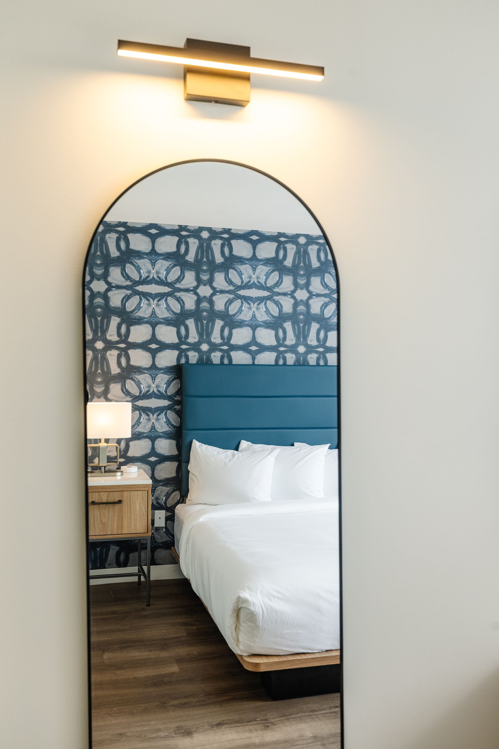 A full length mirror in a hotel room shows a bed.