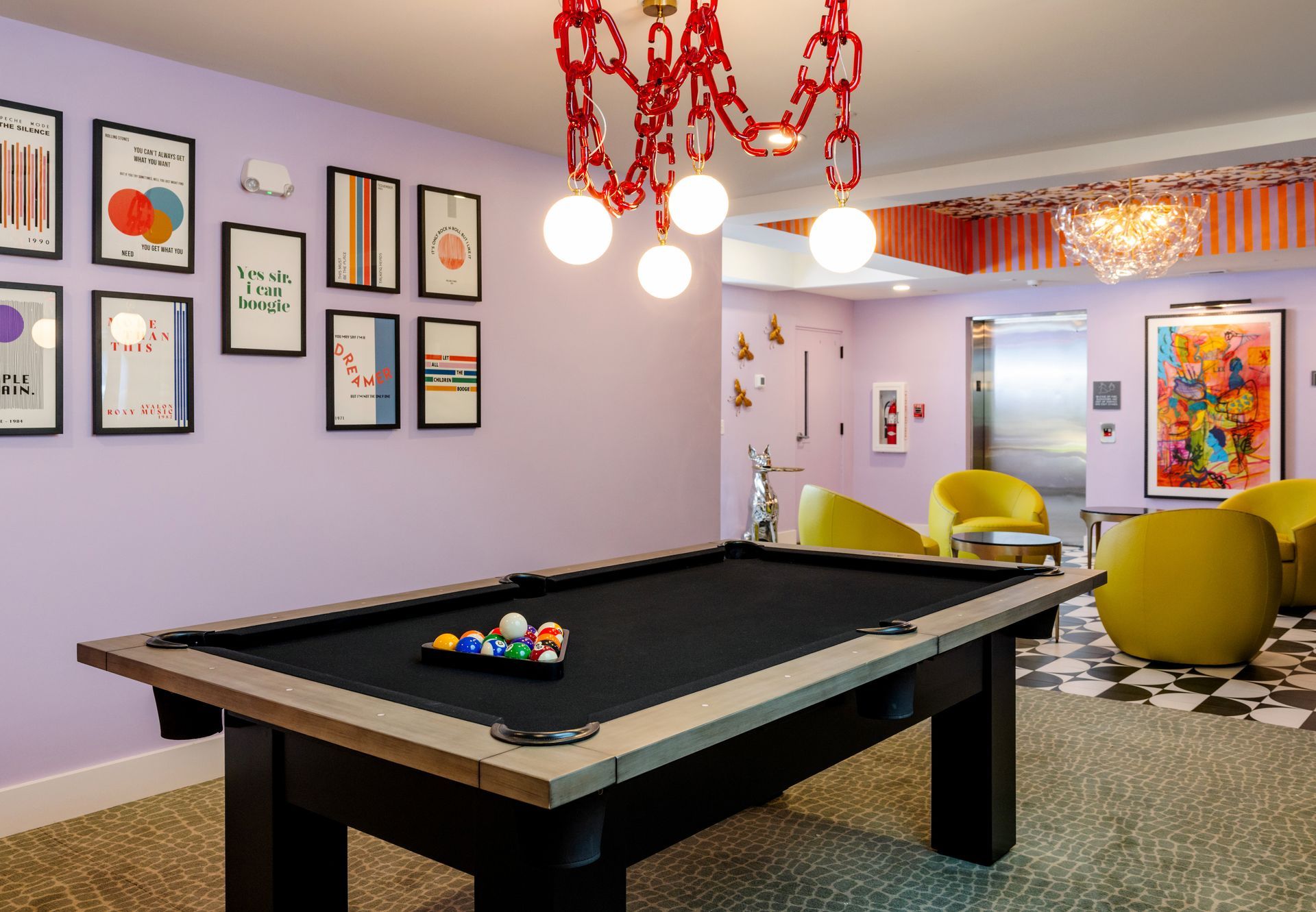 A pool table in a room with purple walls and yellow chairs
