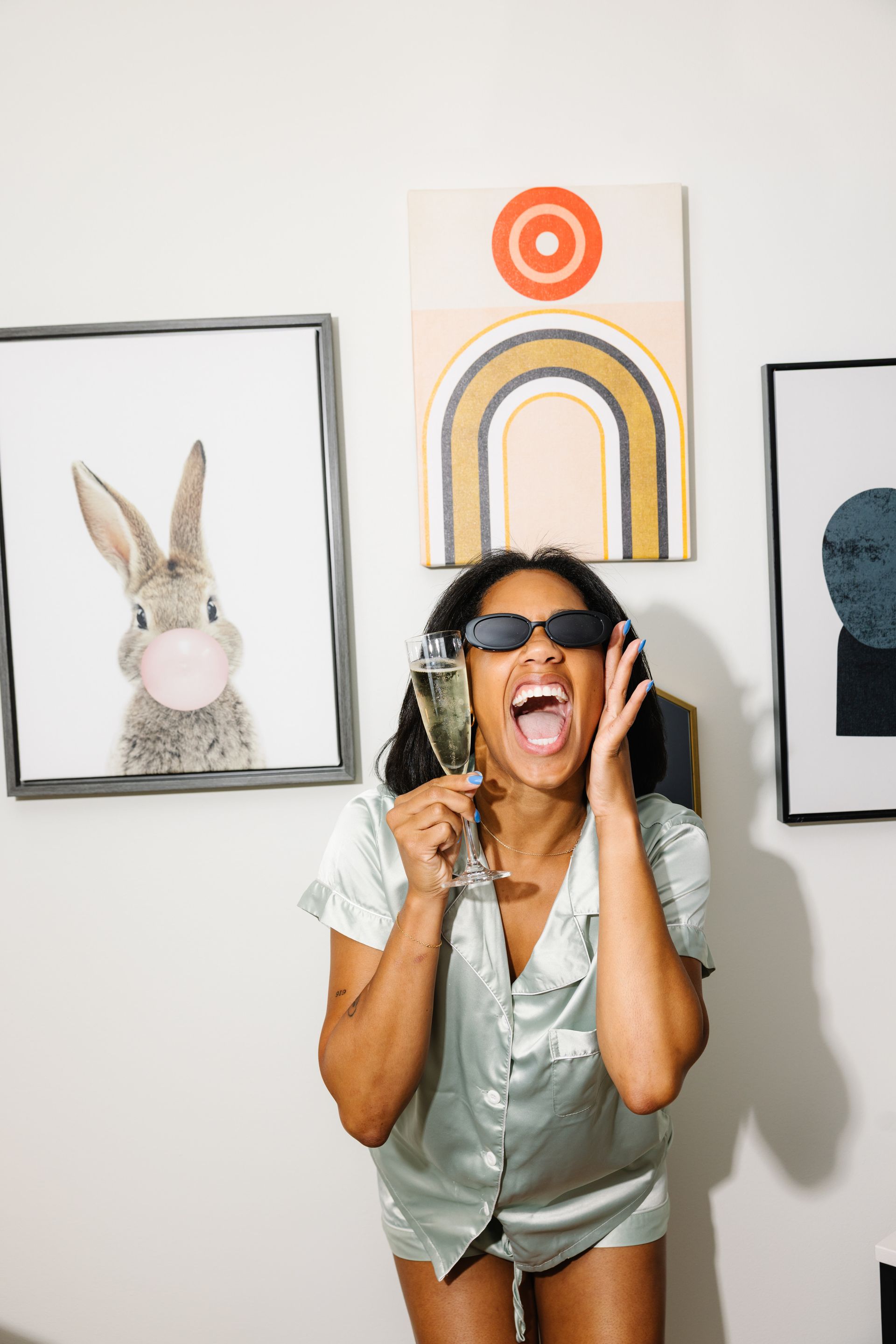 A woman is holding a glass of champagne in front of a wall with paintings.