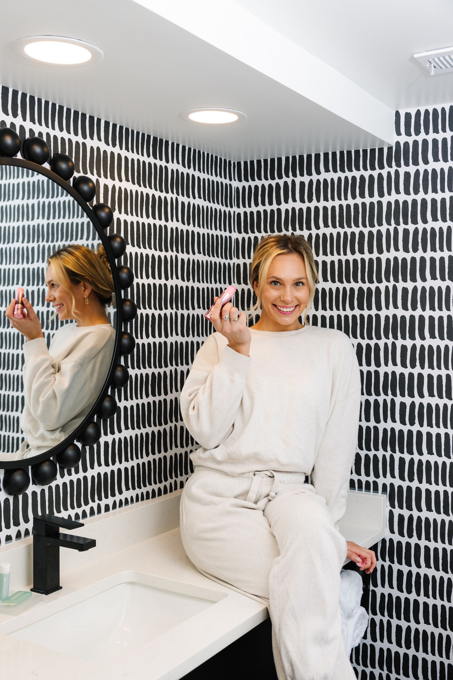 A woman is sitting on a counter in front of a mirror in a bathroom.