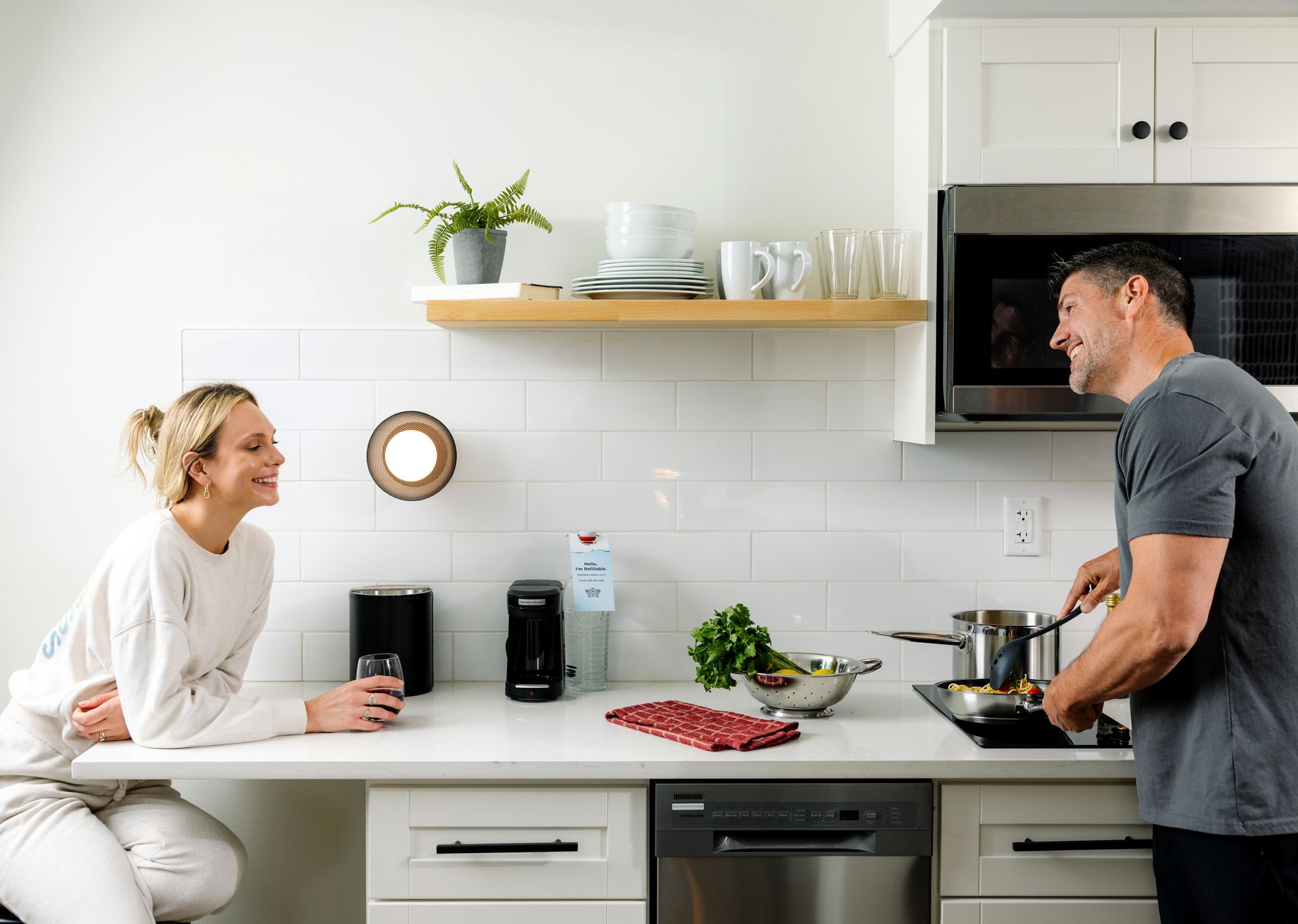 A man is cooking in a kitchen while a woman sits at a counter.