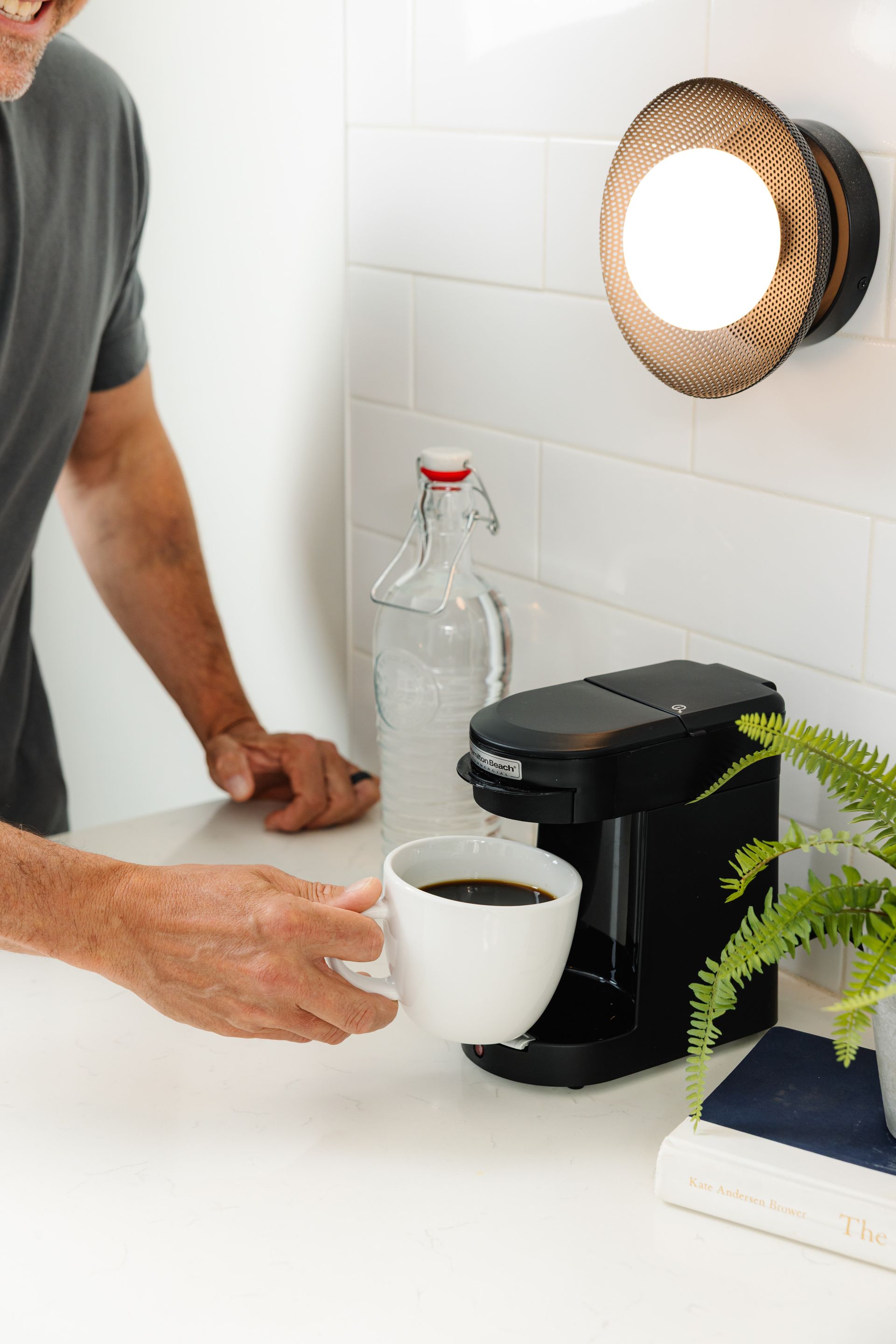 A man is holding a cup of coffee next to a coffee maker.