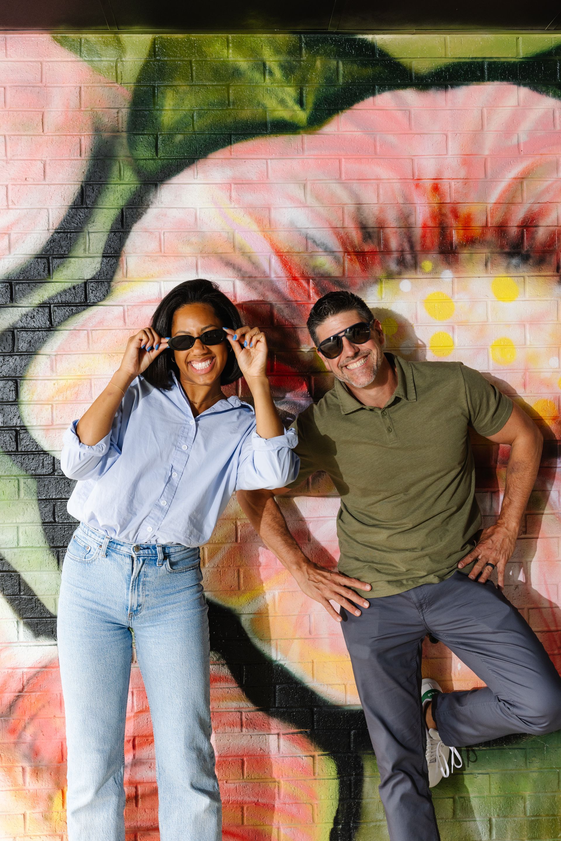 A man and a woman are standing in front of a mural on a brick wall.