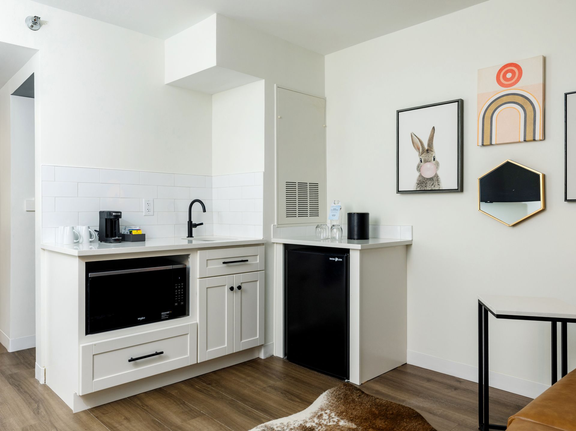 A kitchen with white cabinets , a black refrigerator , a microwave , and a sink.