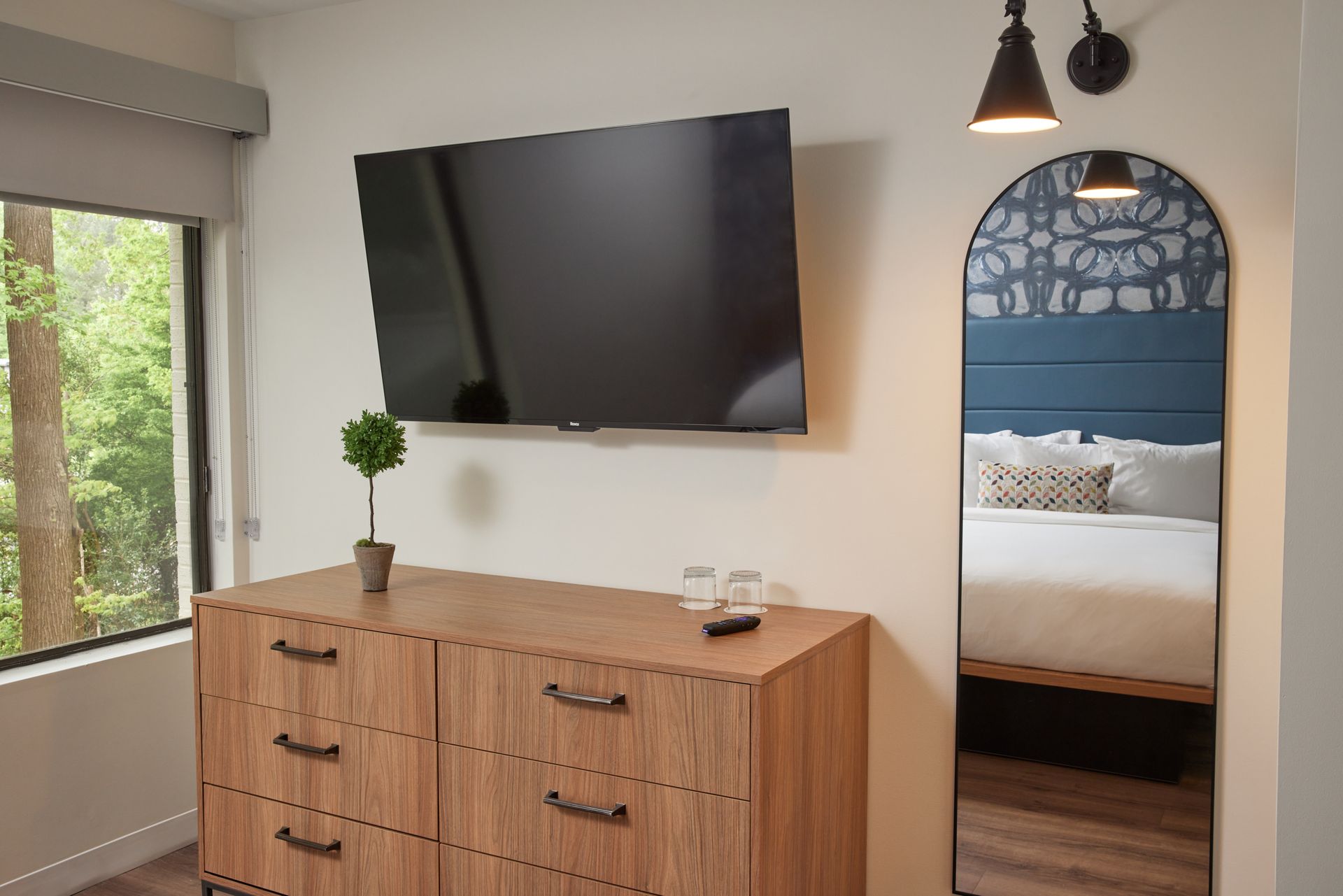 A hotel room with a dresser , television , and mirror.