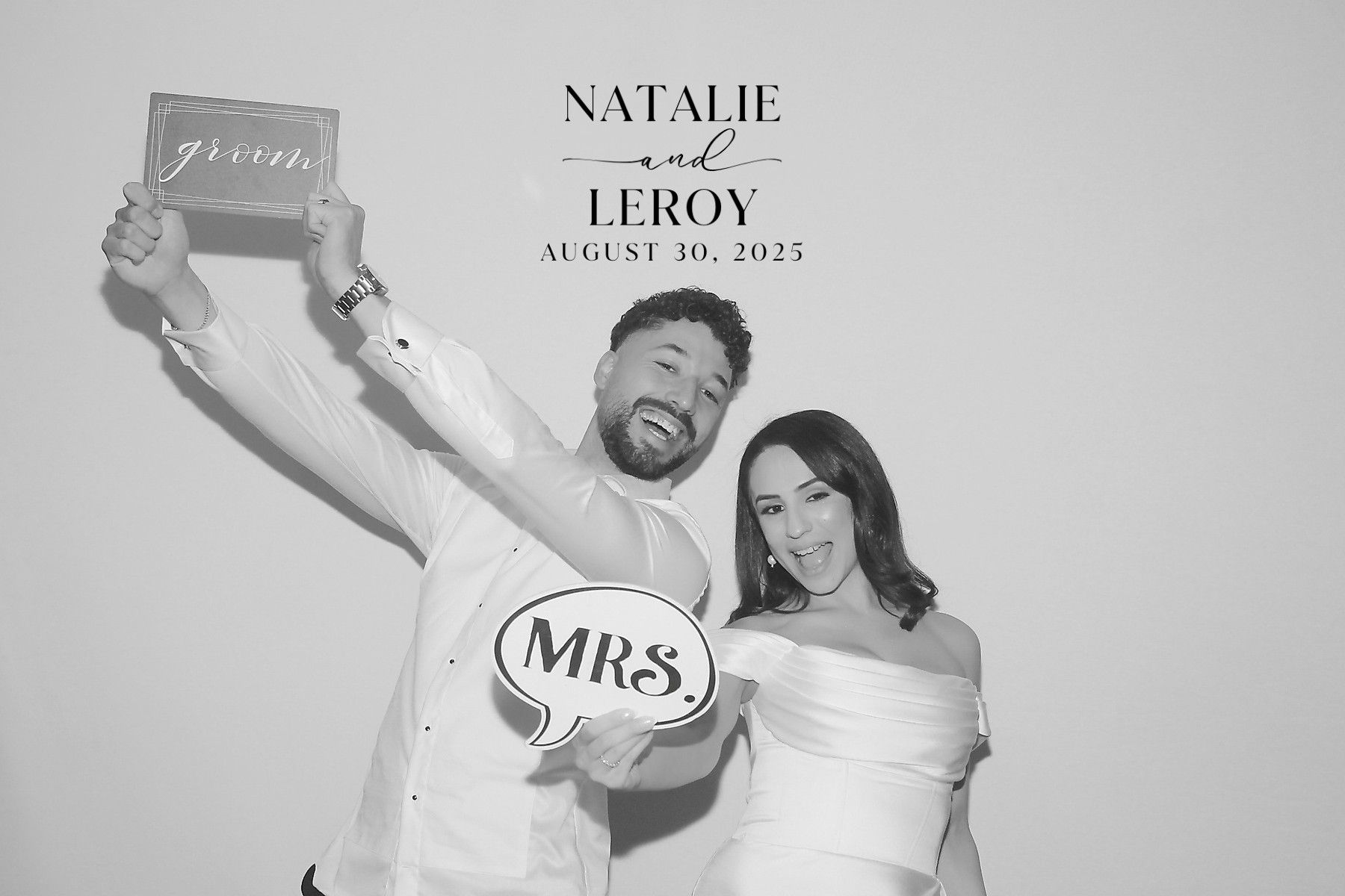 A couple poses for a photo at their wedding, holding signs that say 