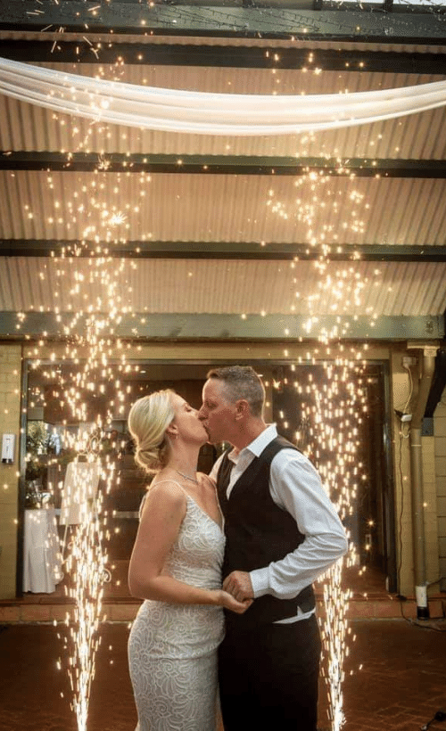 Bride and groom kiss under a sparkler archway at an outdoor wedding venue.