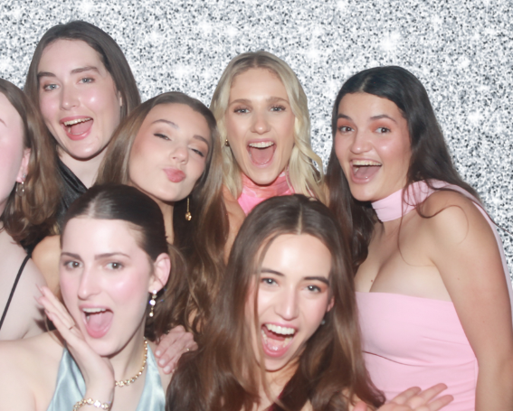 Group of smiling people posing for a photo; some wearing sunglasses, smiles, and hats in a well-lit room.