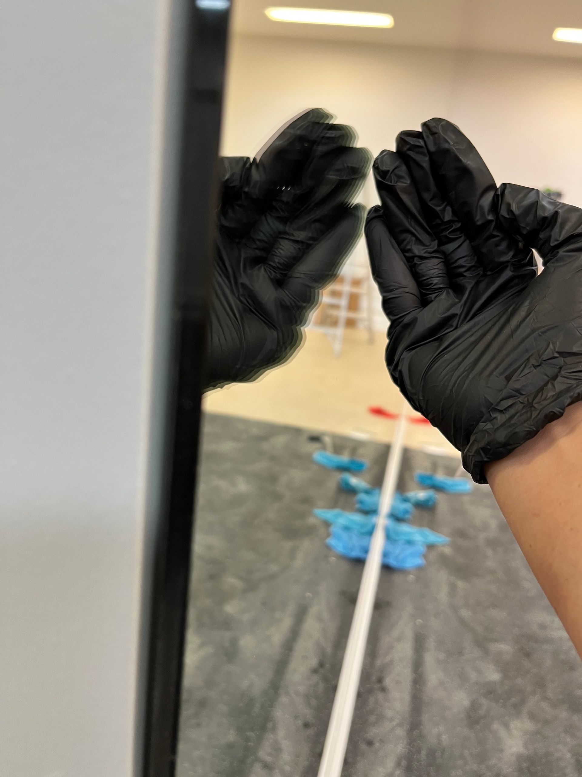 A person wearing black gloves is standing in front of a mirror.