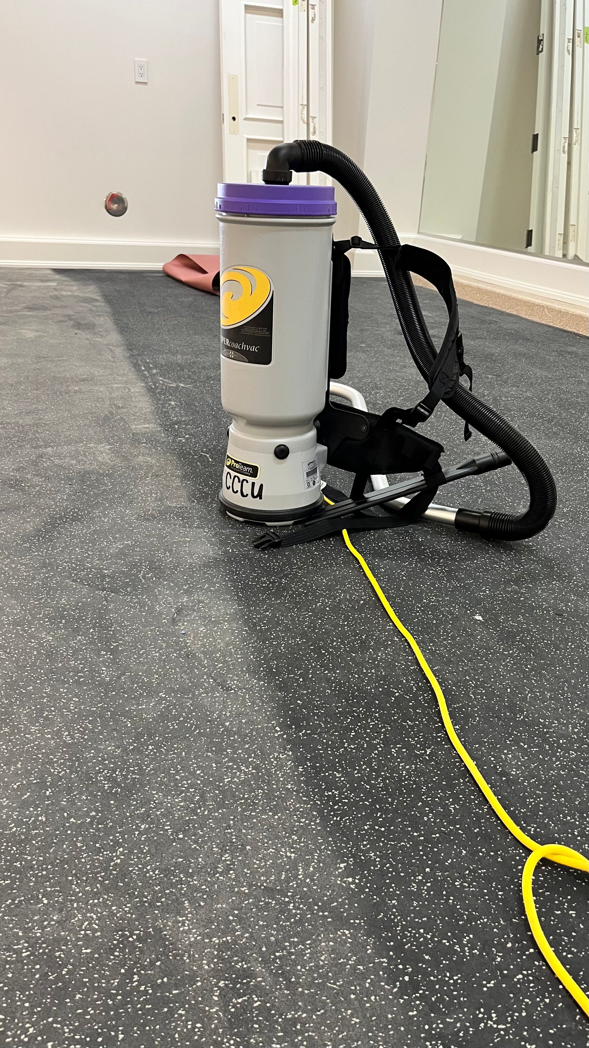 A vacuum cleaner is sitting on a gym floor next to a yellow cord.