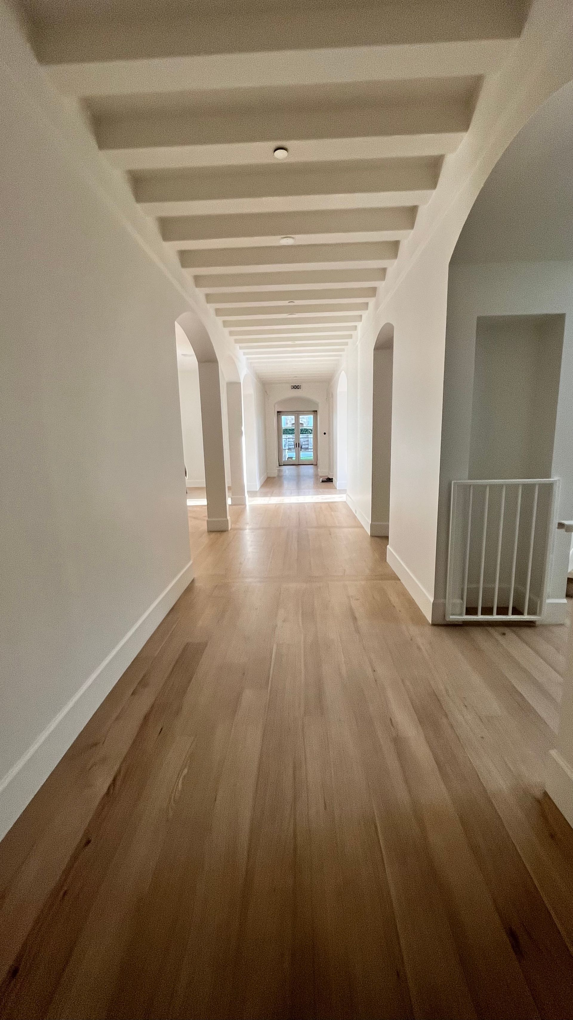 A long hallway with wooden floors and white walls in a house.