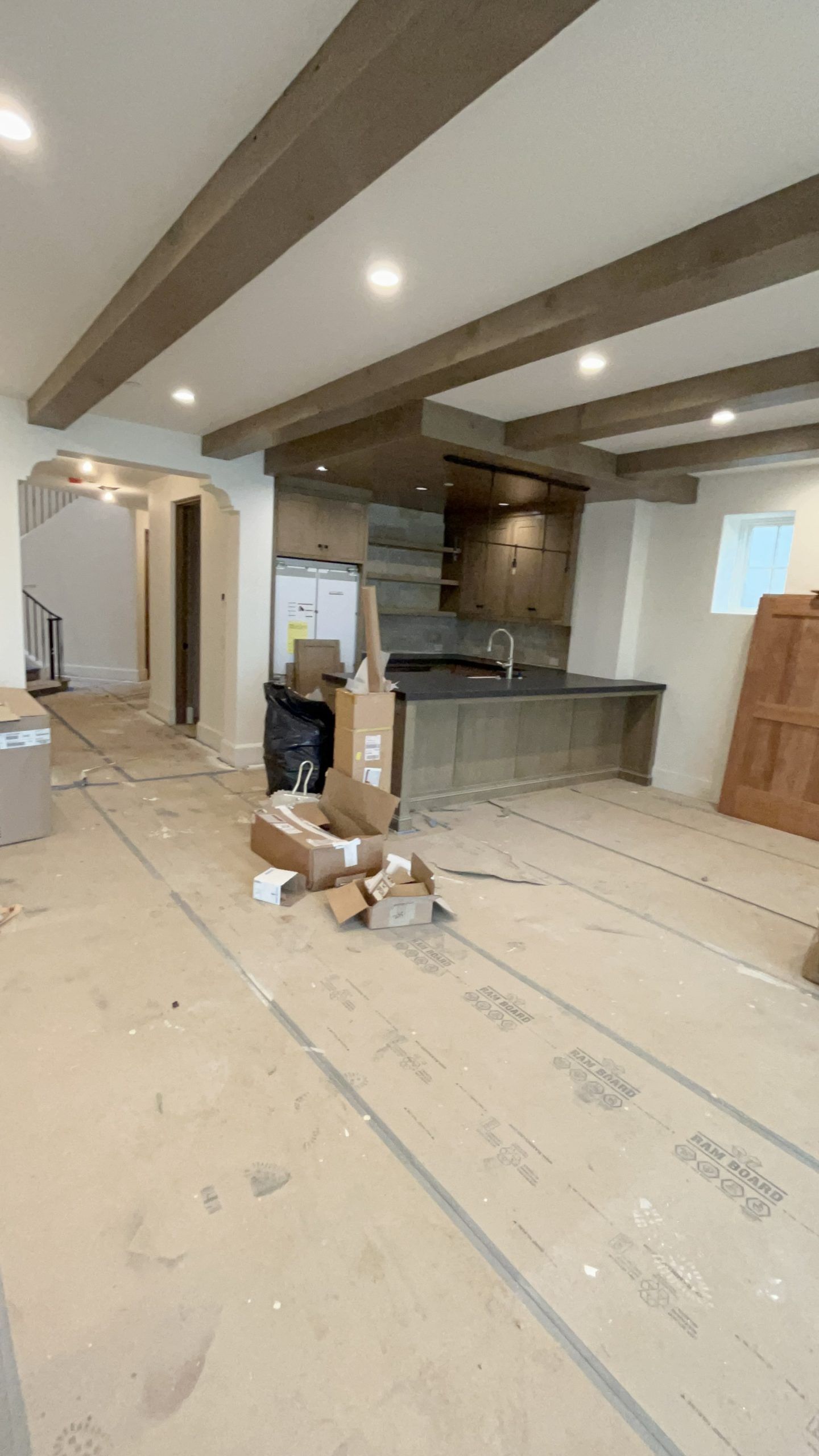 A room with a lot of boxes on the floor and a kitchen in the background.