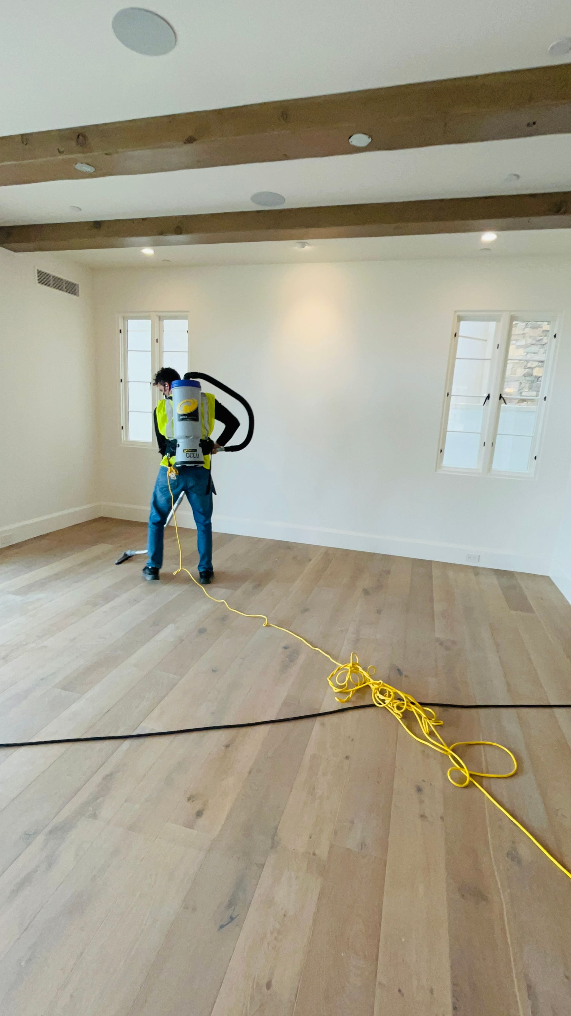 A man is standing in an empty room with a vacuum cleaner on his back.