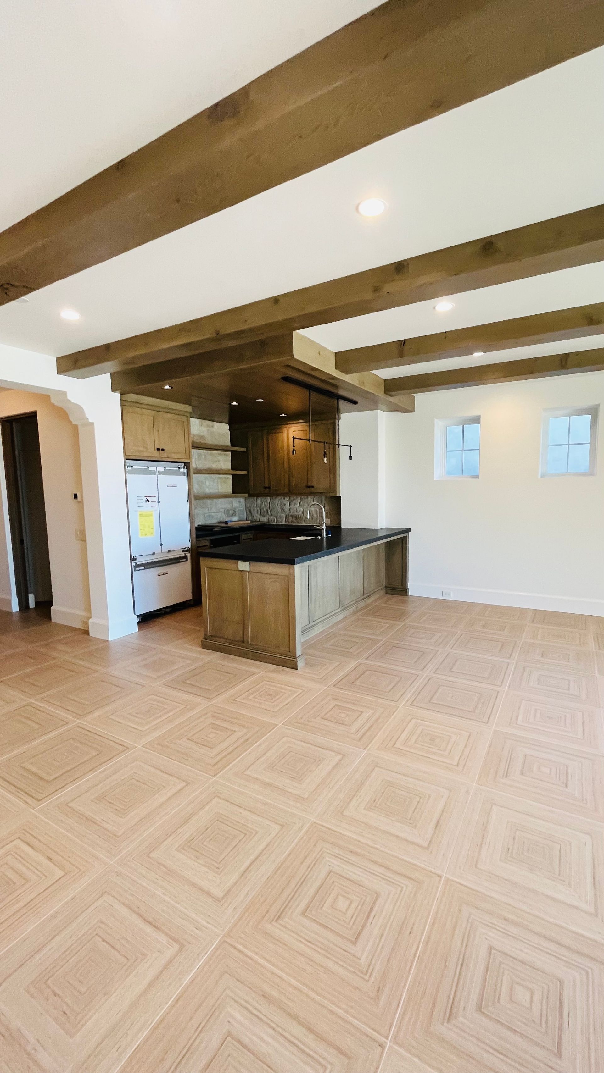 A large empty room with a kitchen in the background and wooden beams on the ceiling.