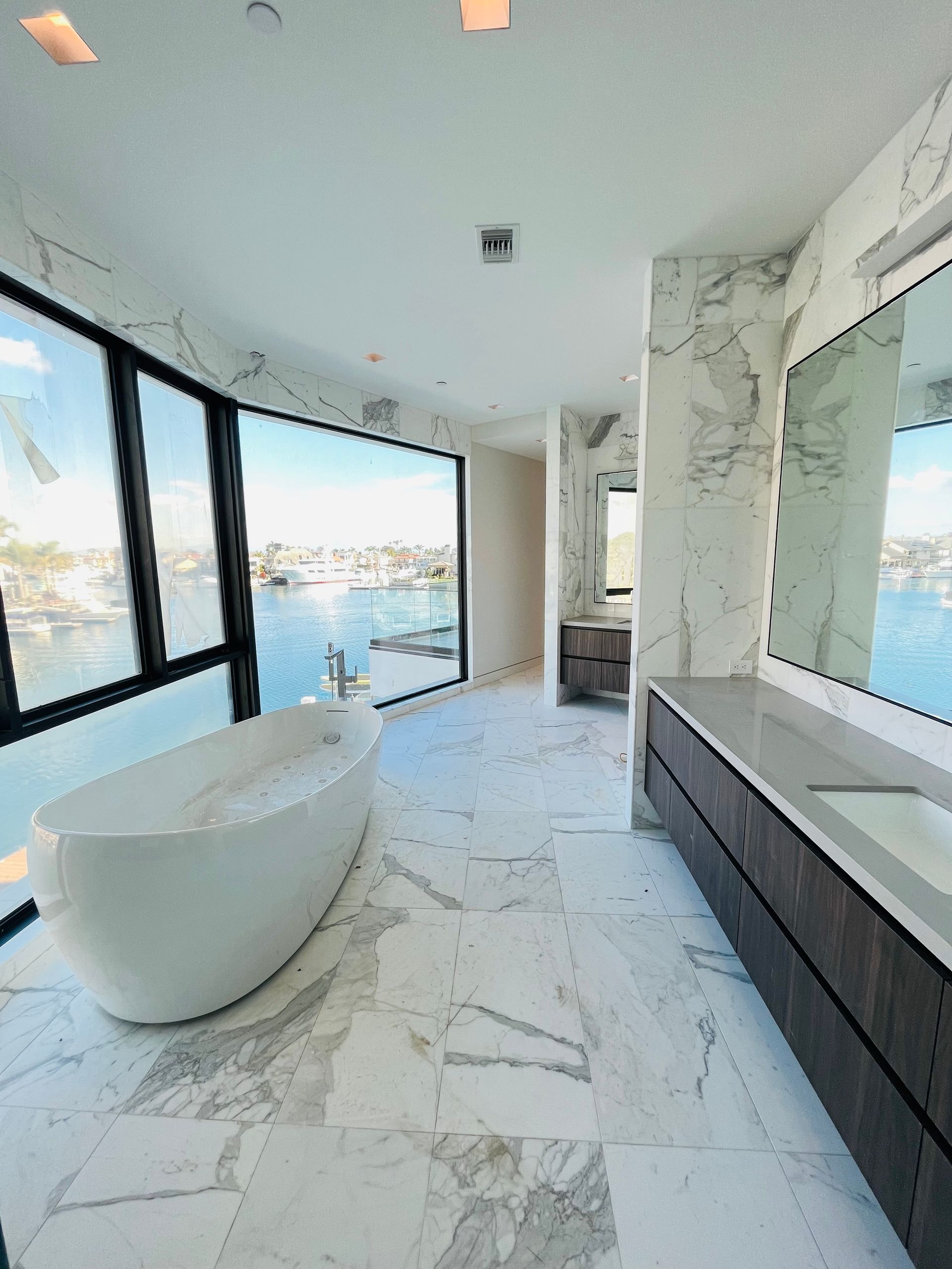 A bathroom with a bathtub , sink , mirror and large windows.