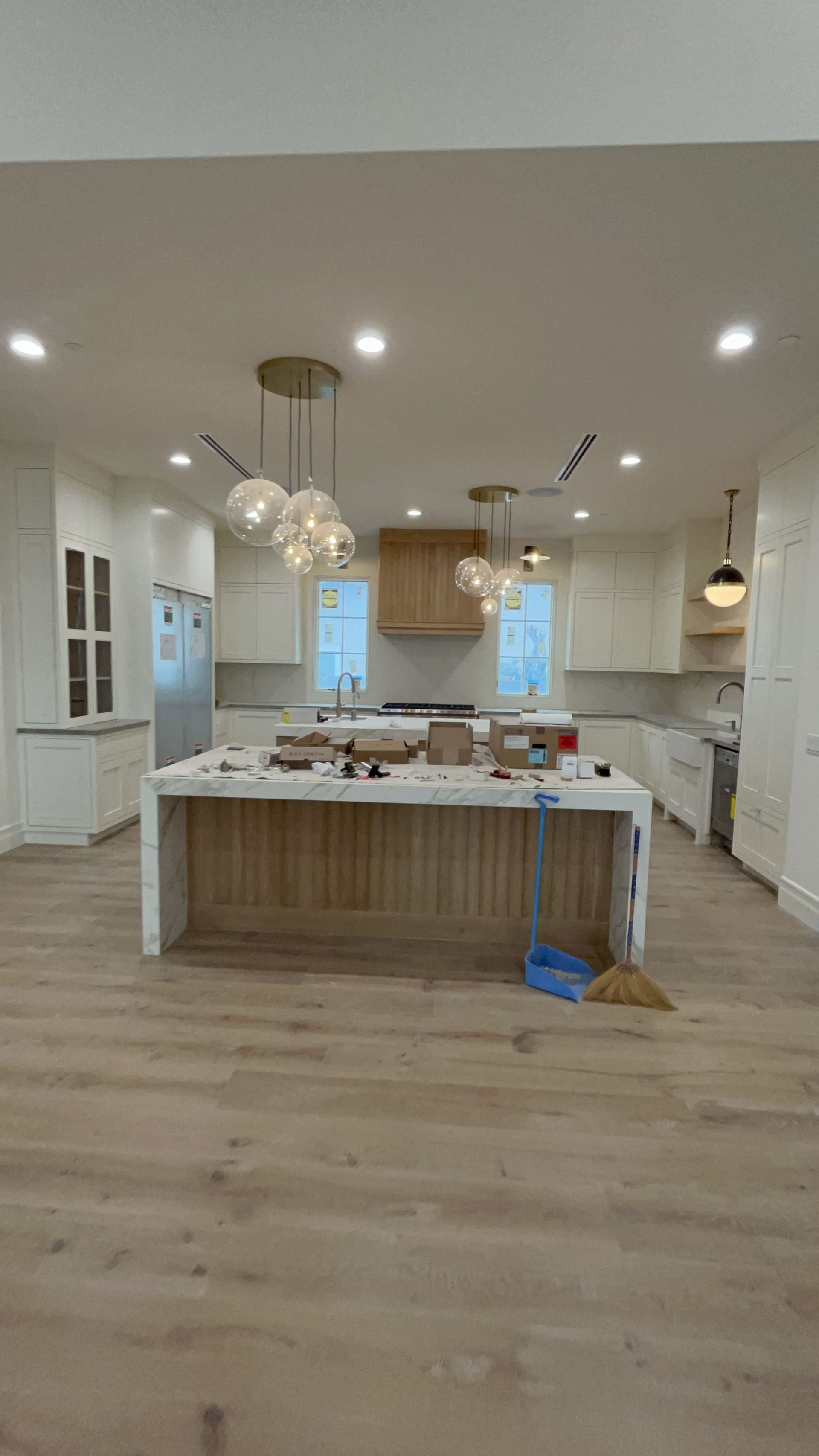 A room with a lot of boxes on the floor and a kitchen in the background.