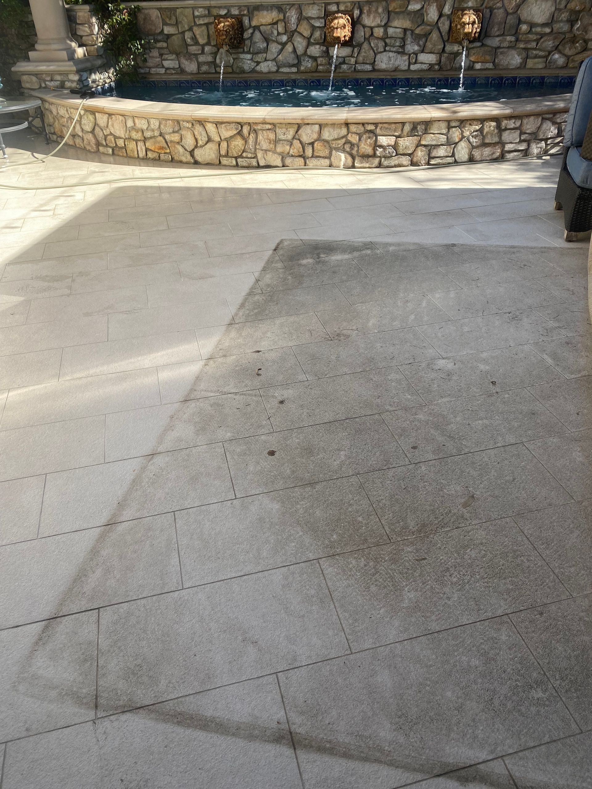A patio with a stone wall and a fountain in the background.