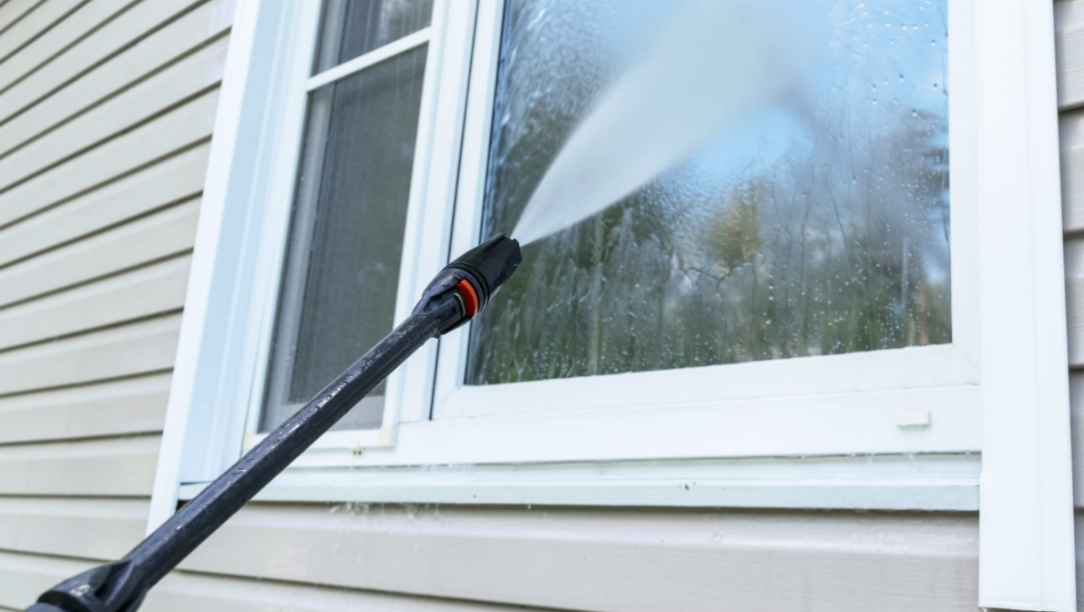 A person is cleaning a window with a high pressure washer.