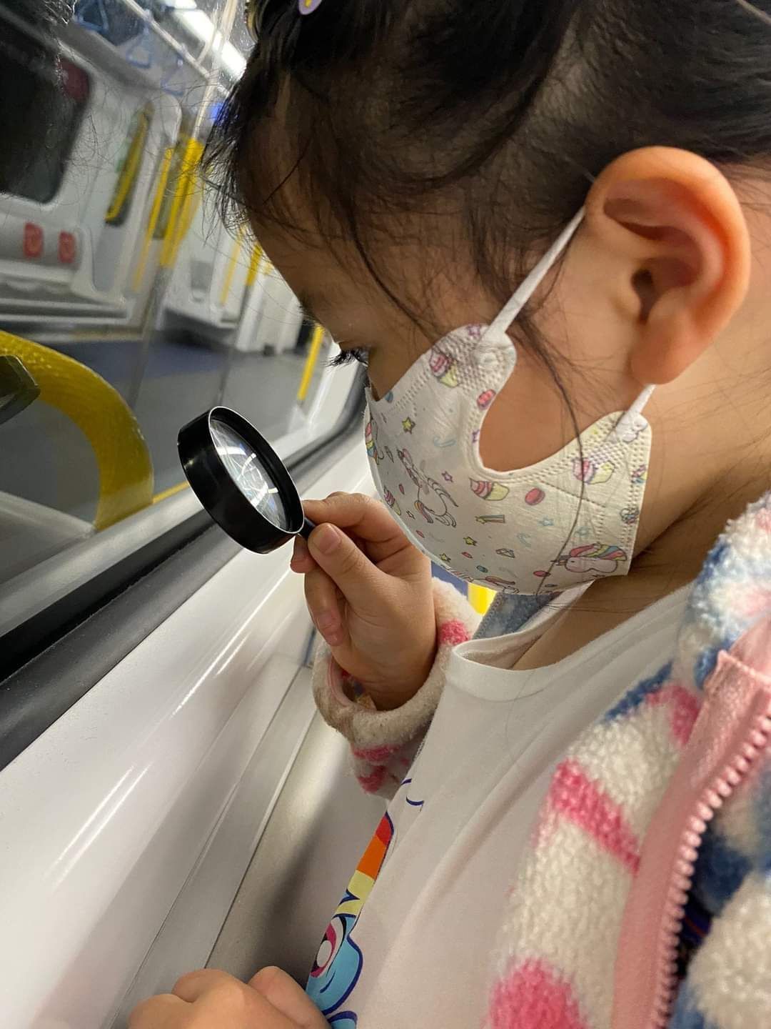 A little girl wearing a mask is looking through a magnifying glass.