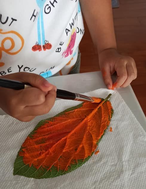 A child is painting a leaf with orange paint