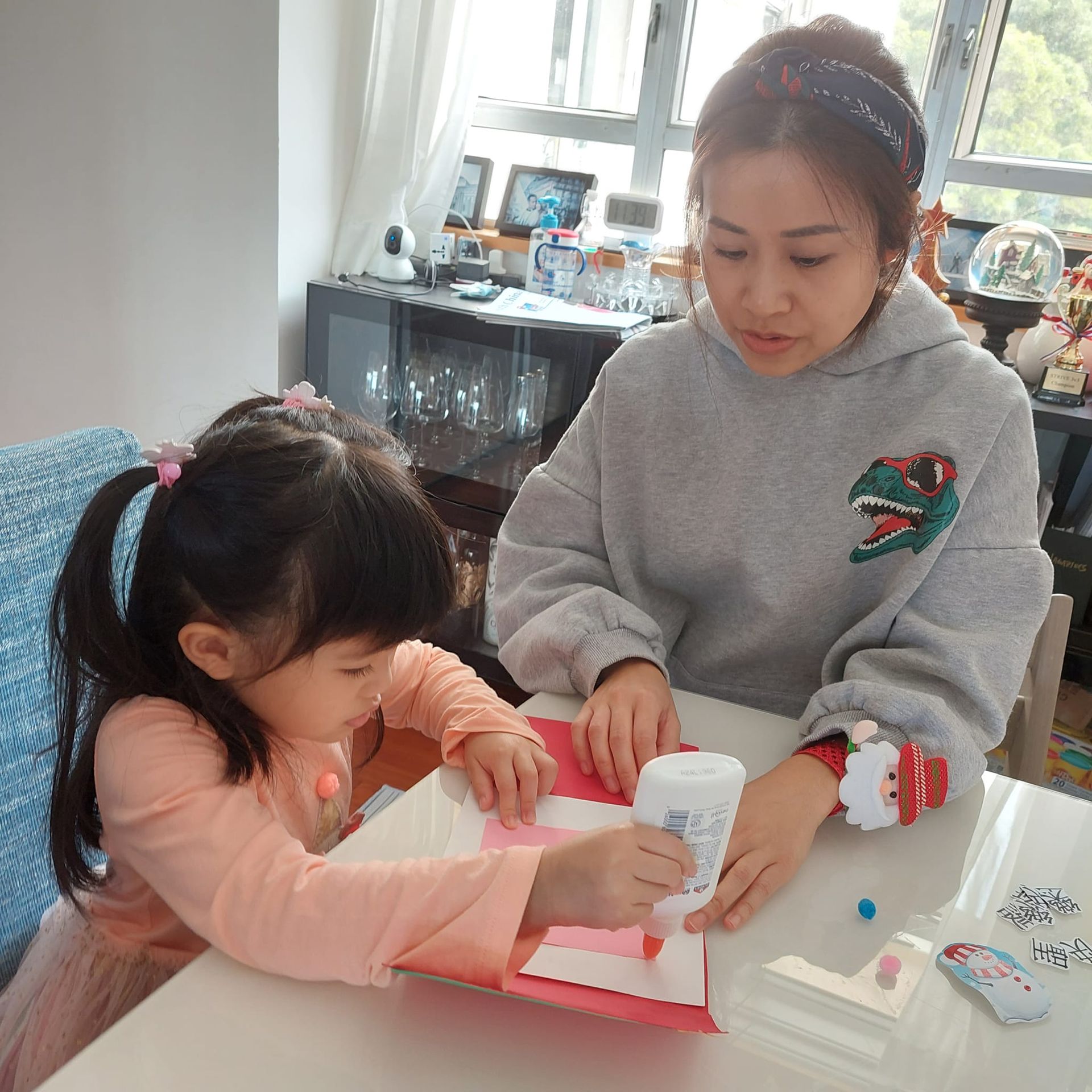 A woman and a little girl are sitting at a table playing with glue.