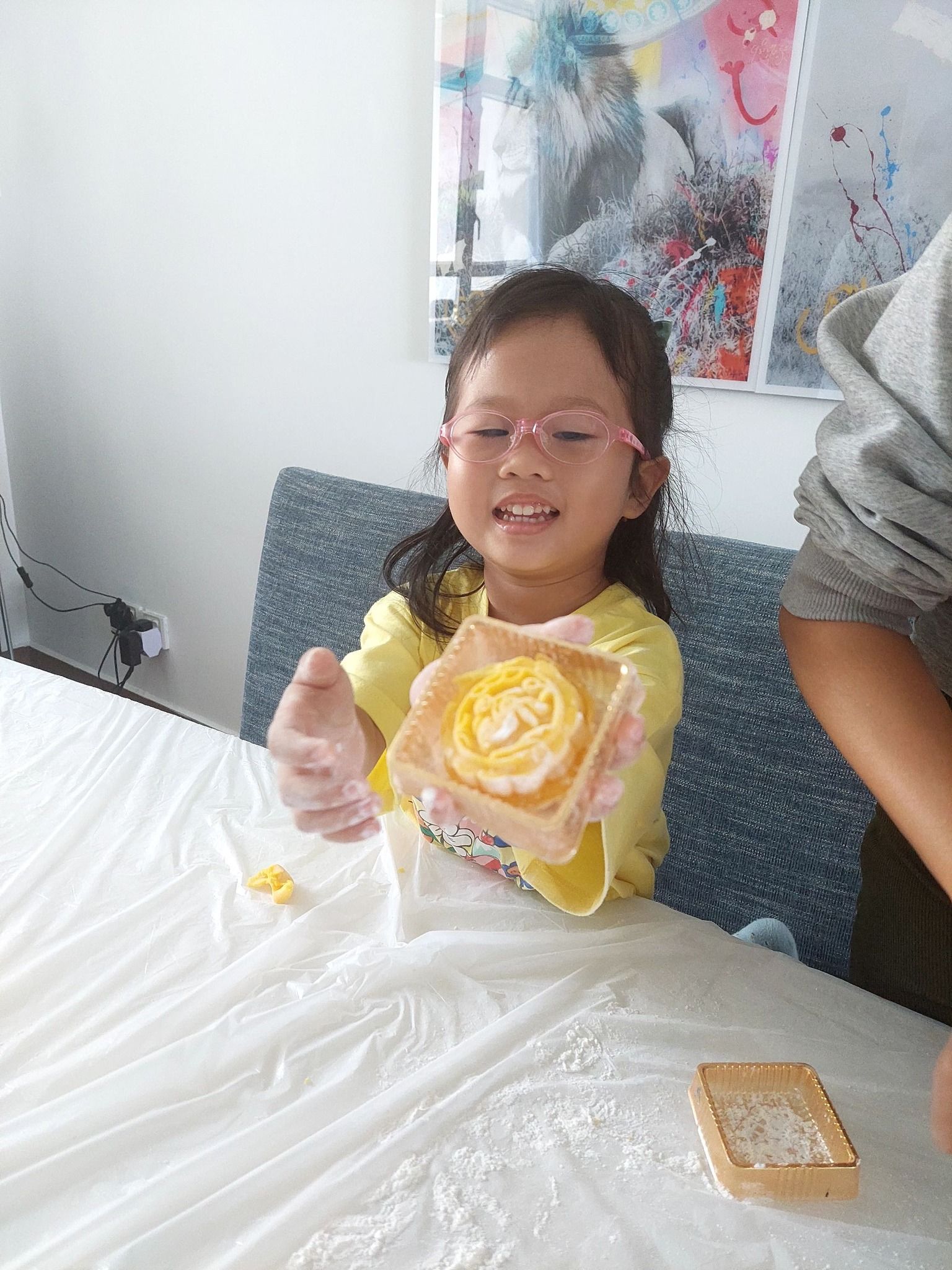 A little girl is sitting at a table holding a flower.