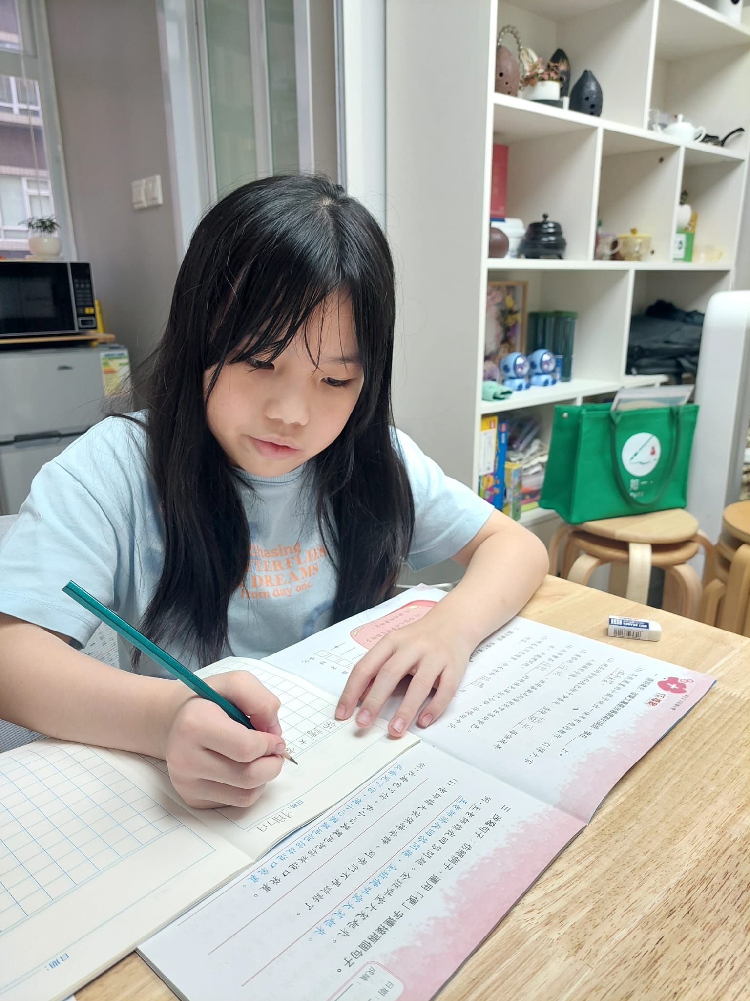 A young girl is sitting at a table writing in a notebook.