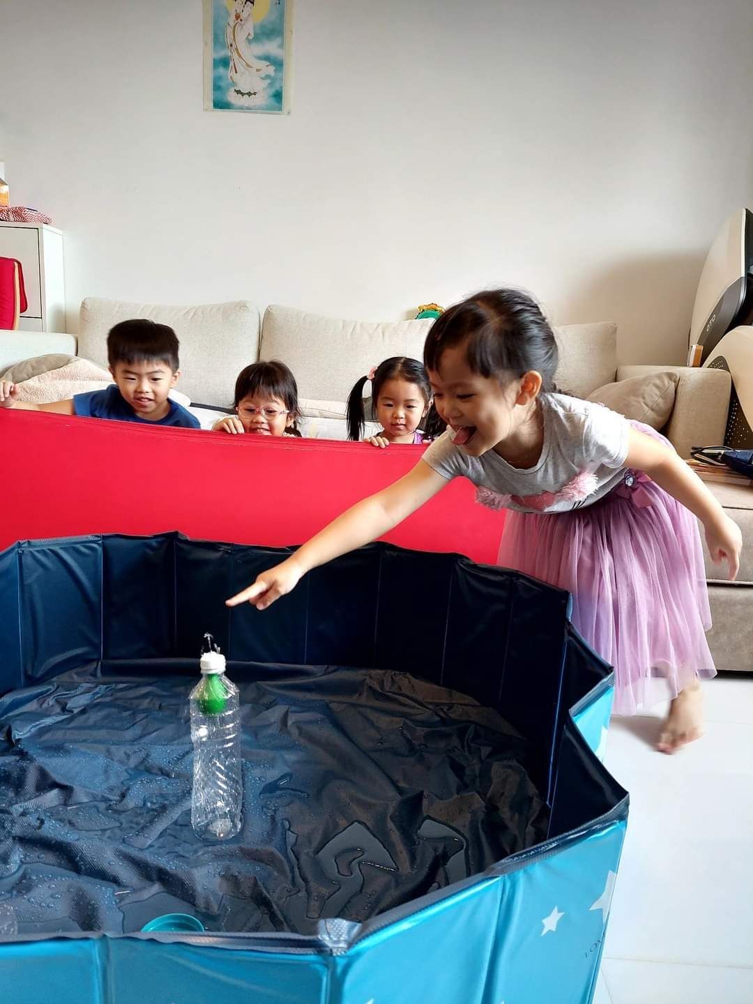 A little girl is pointing at a bottle in a pool of water.
