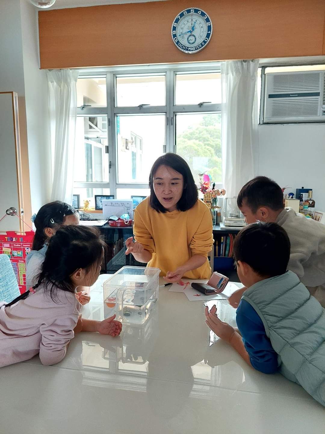 A woman is sitting at a table with a group of children.