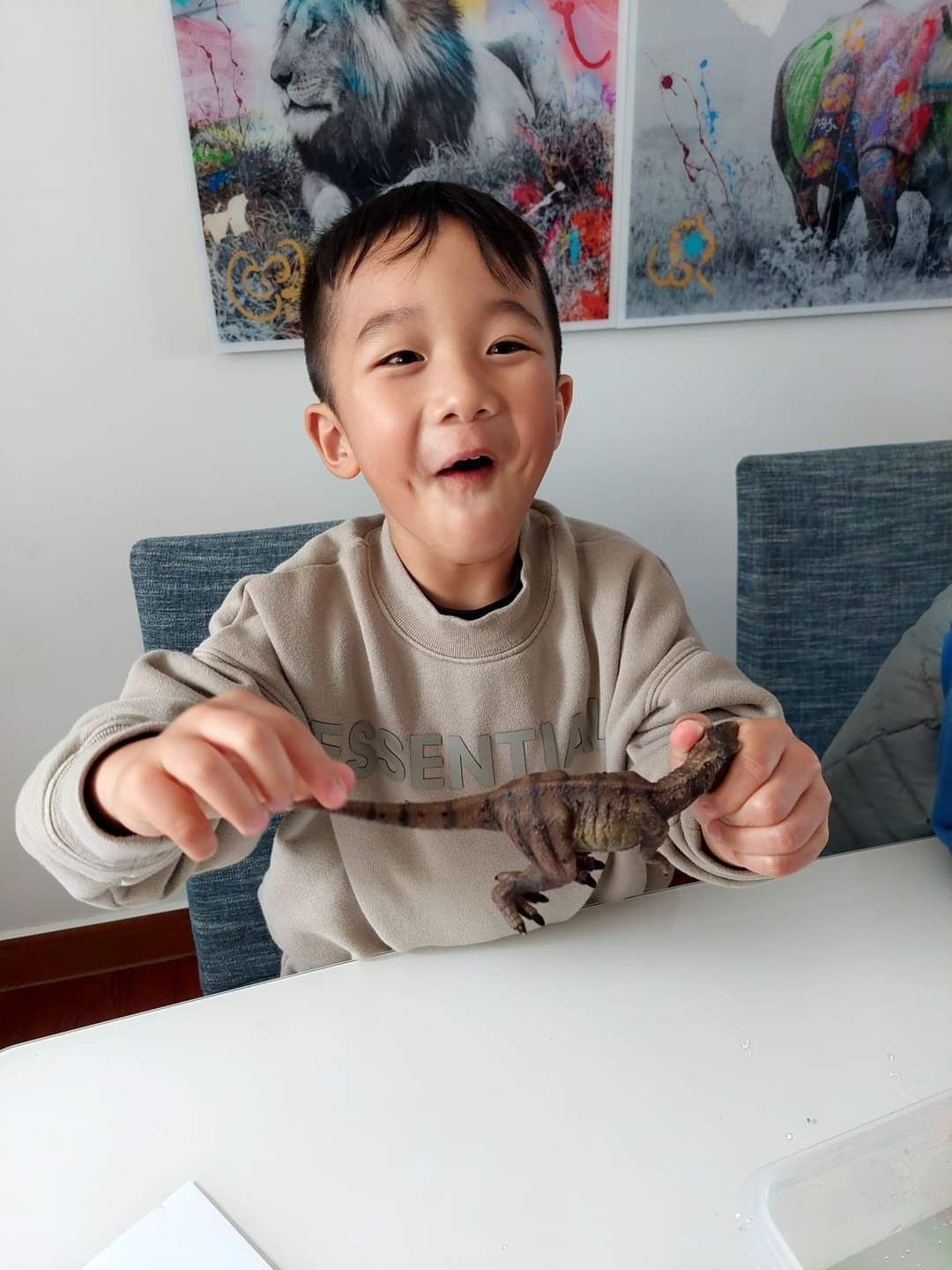 A young boy is sitting at a table holding a toy dinosaur.