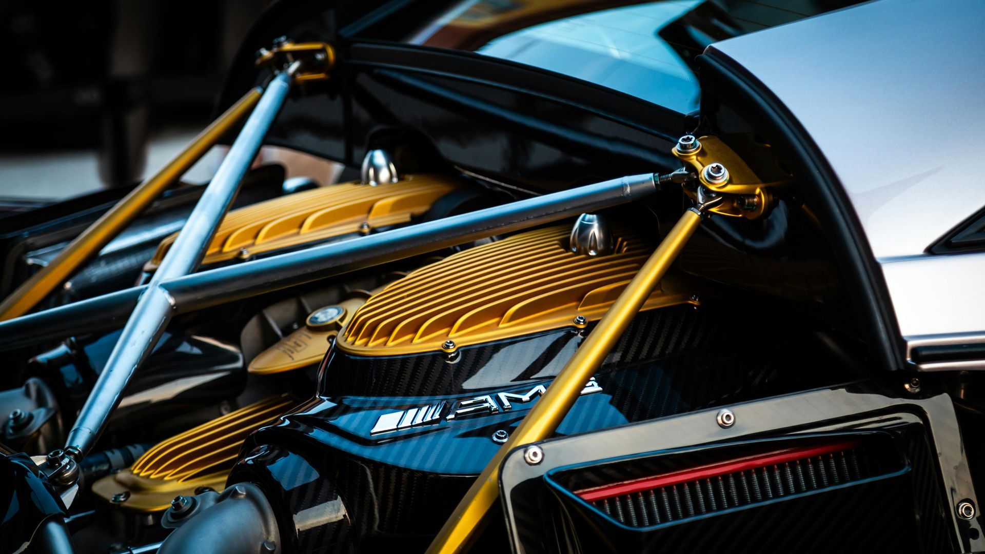 Close-up of a luxury car's engine bay with gold struts and heat shields, set against carbon fiber.