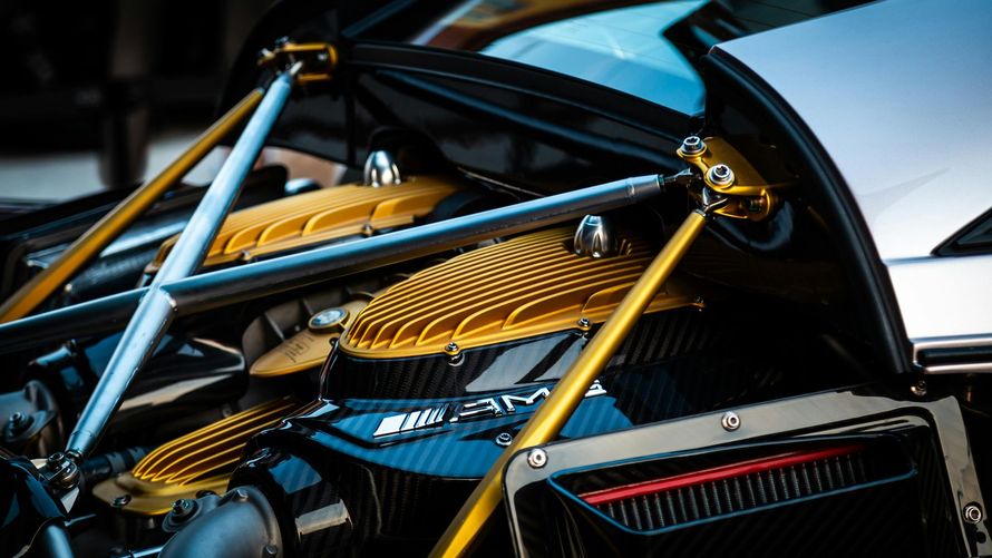 Close-up of a luxury car's engine bay with gold struts and heat shields, set against carbon fiber.