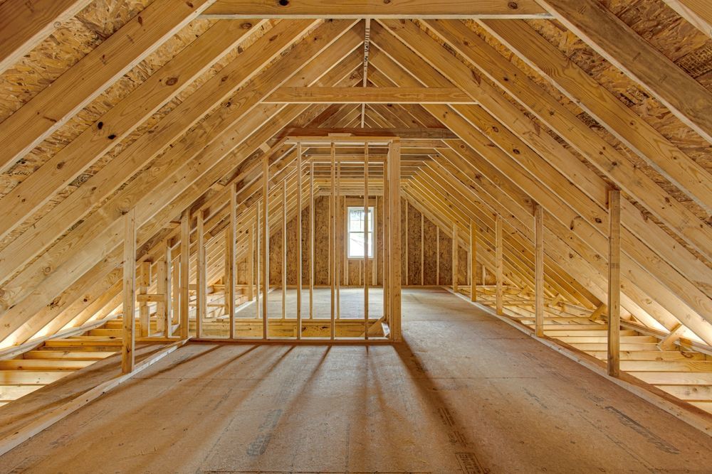 Interior of an unfinished wooden attic with exposed roof framing and a small window at the far end.