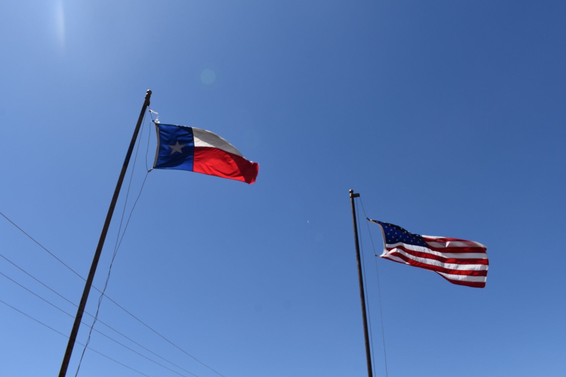 Two flags are waving in the wind against a blue sky.
