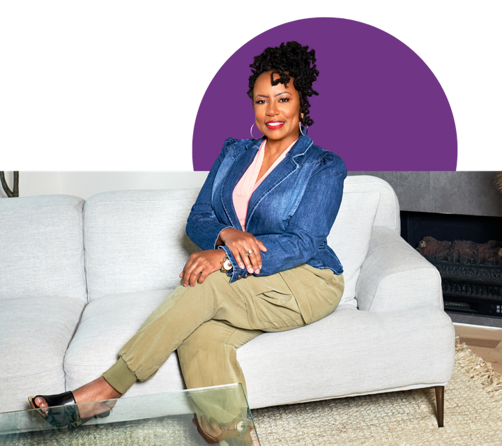 Woman seated on a light grey couch, wearing a blue jean jacket and khaki pants. Purple semi-circle behind her.