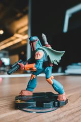 A Boba Fett action figure with blue armor and a green cape, standing on a black base on a wooden surface.