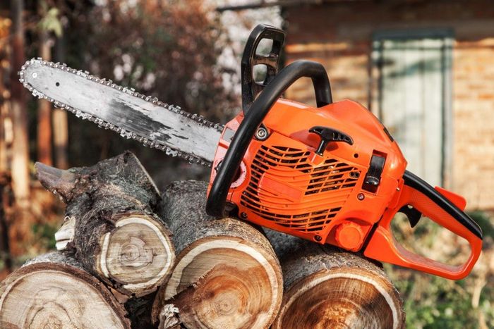 Orange chainsaw resting on a pile of cut firewood, outdoors.
