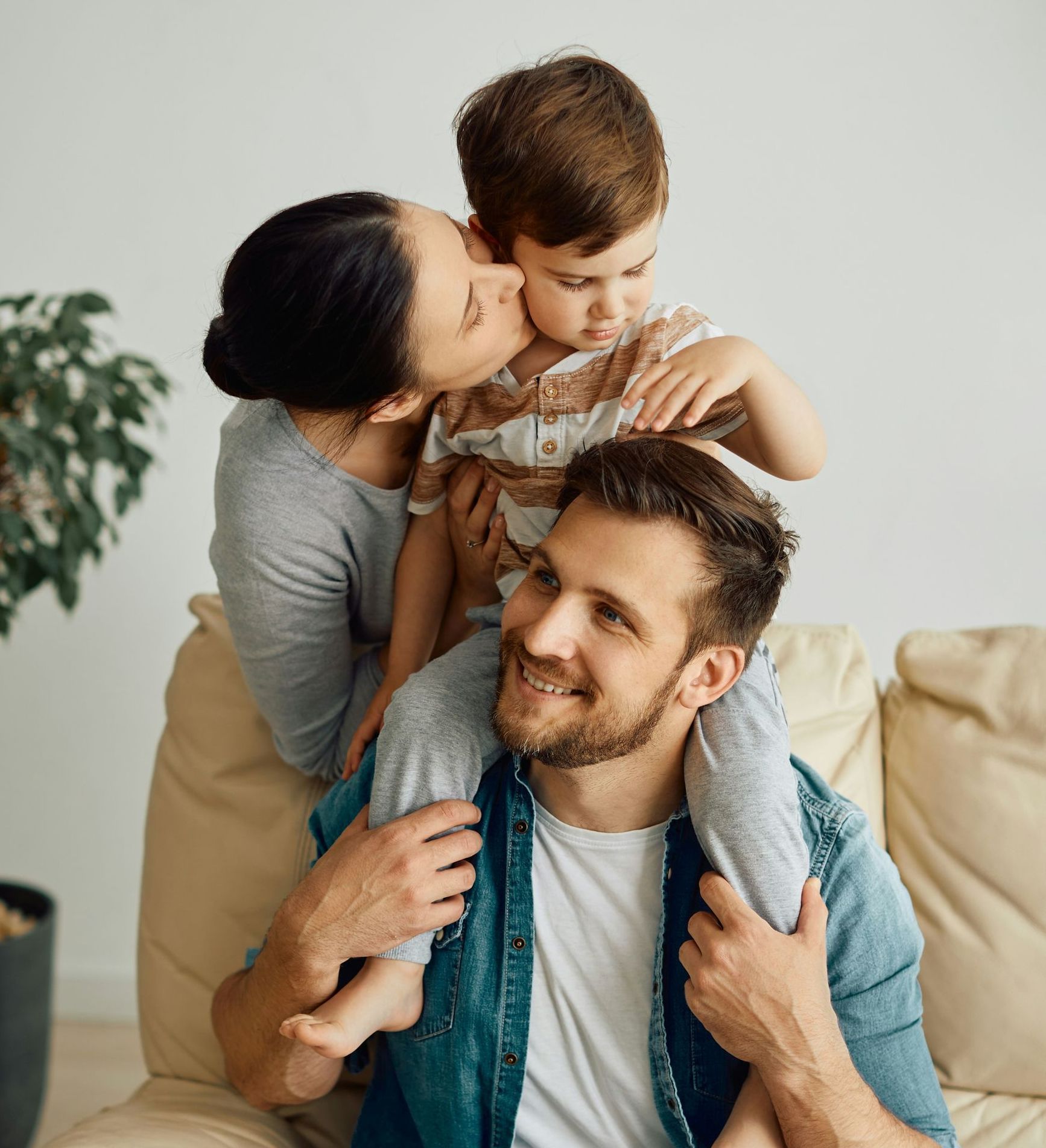 A man and a woman are sitting on a couch with a child on his shoulders.