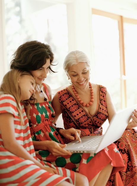Family of three looking at a laptop: a girl, a woman, and an older woman smiling. Indoors.