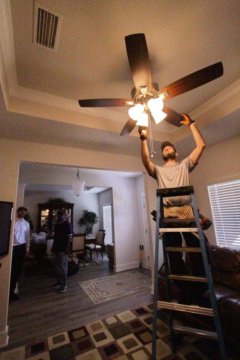 A man is standing on a ladder fixing a ceiling fan in a living room - Milton, FL - Damn Fine Jobs