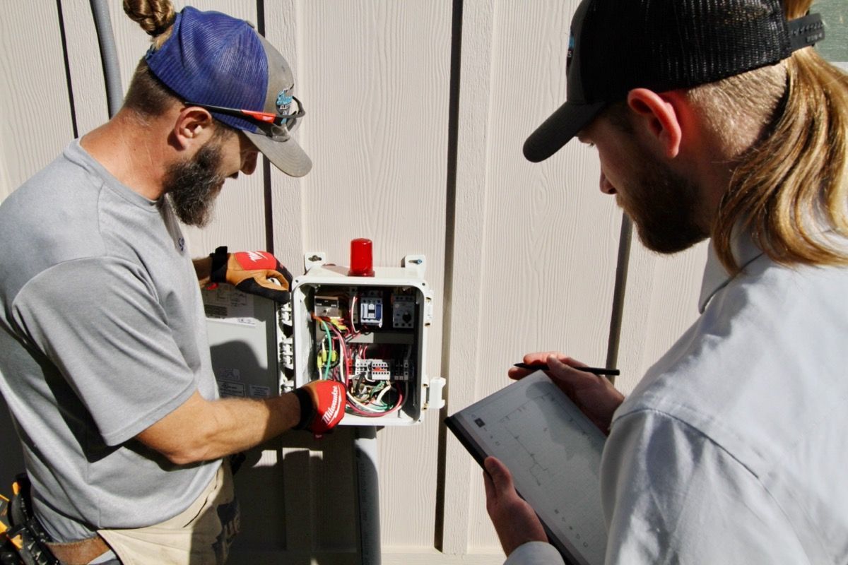 Two men are working on an electrical box while another man looks at a clipboard - Milton, FL - Damn Fine Jobs
