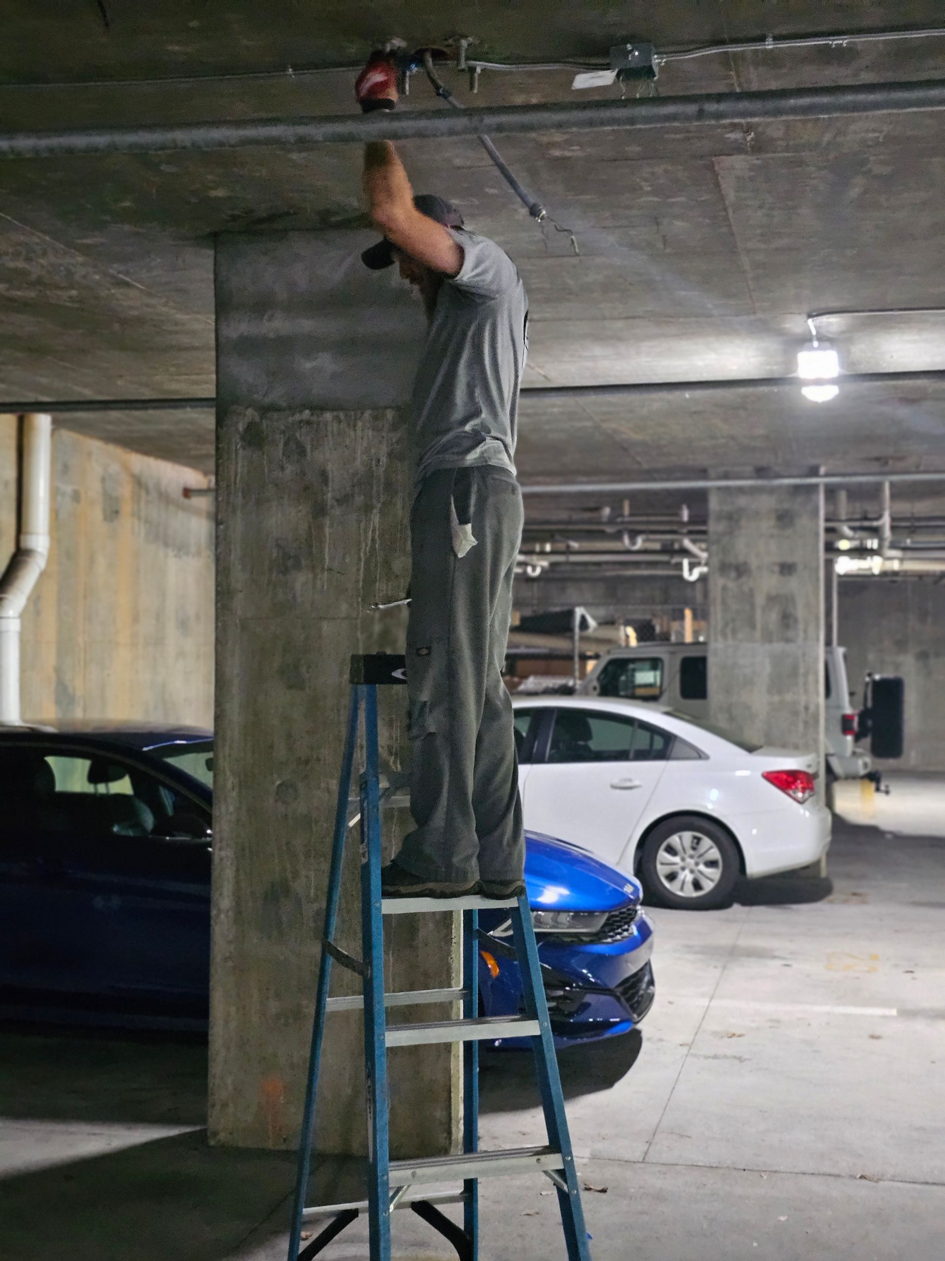 A man is standing on a ladder in a parking garage - Milton, FL - Damn Fine Jobs