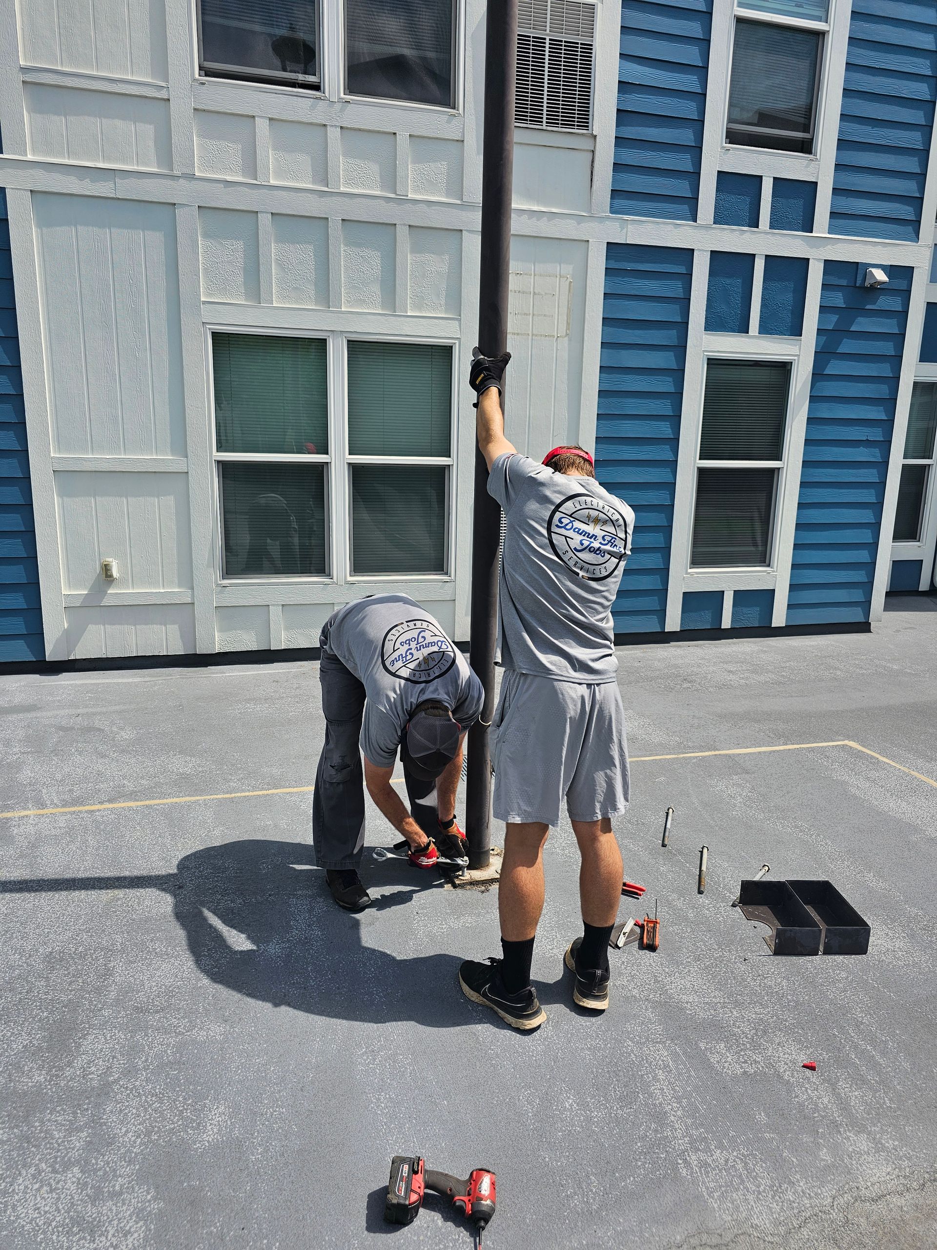 Two men are working on a pole in front of a blue building - Milton, FL - Damn Fine Jobs